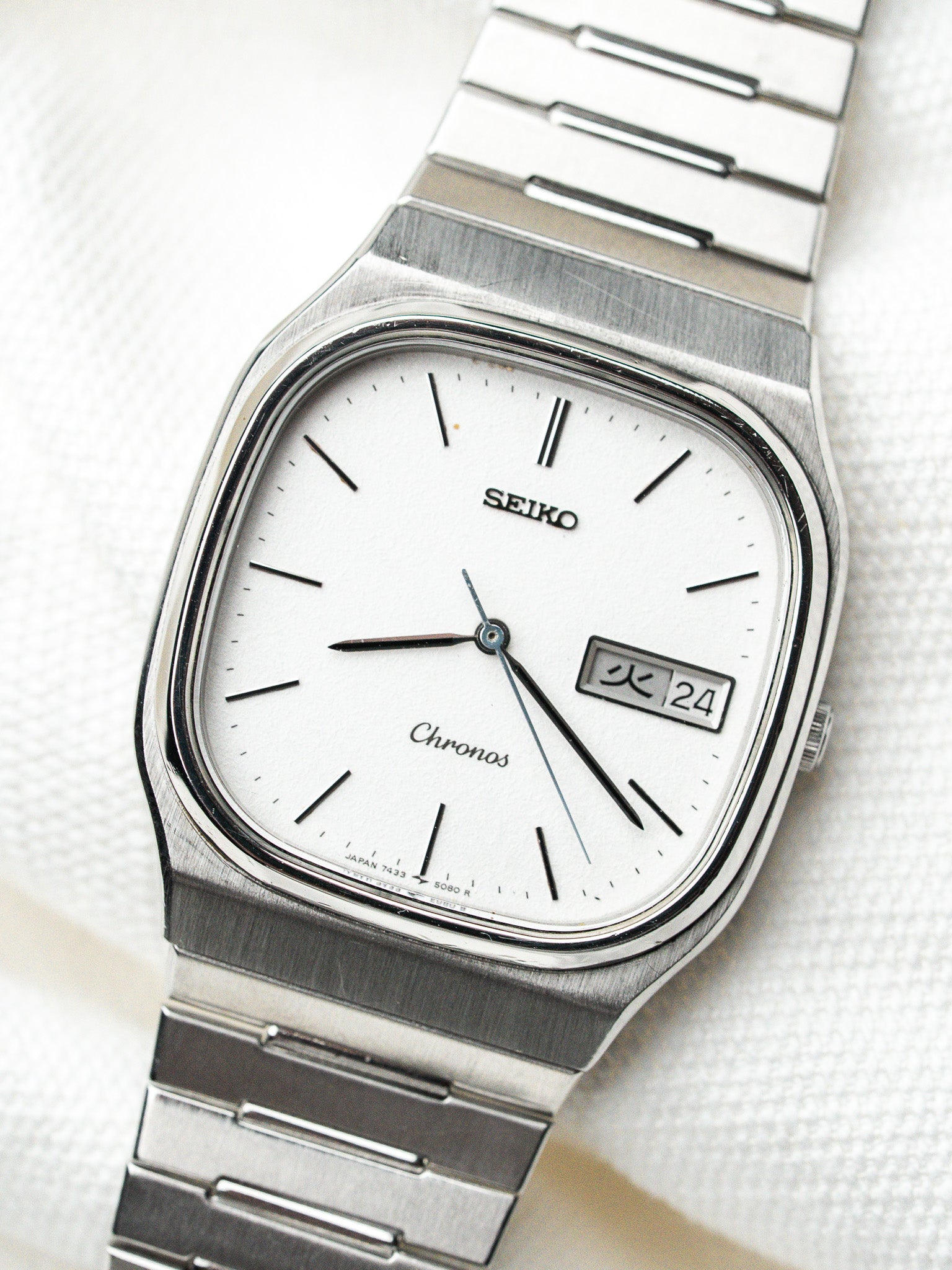Seiko Chronos vintage watch with white dial, steel case, and day-date window on textured background