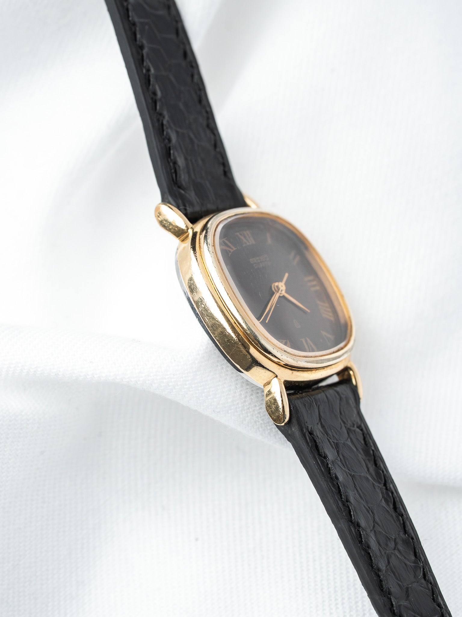 Vintage Seiko watch with gold case, black dial, Roman numerals, and black leather strap