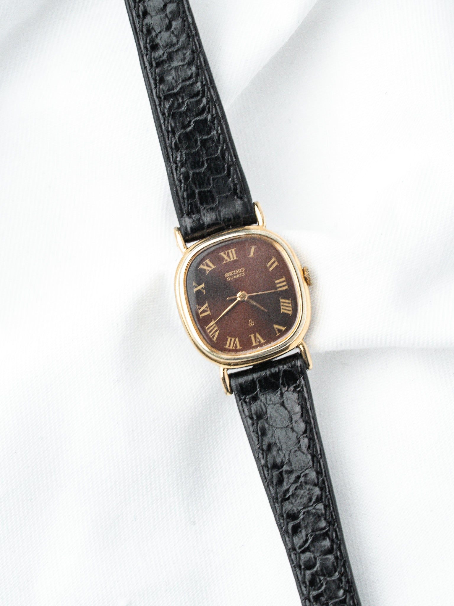 Seiko vintage watch with gold case, brown dial, Roman numerals, black textured strap