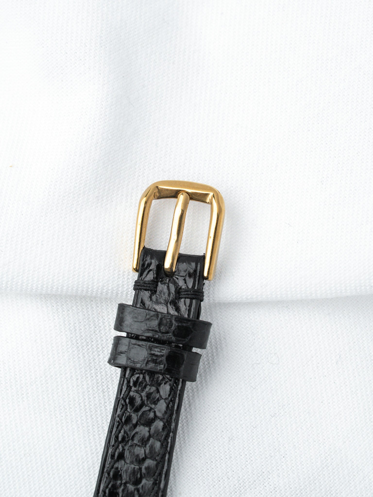 Black alligator leather watch strap with gold buckle on white background