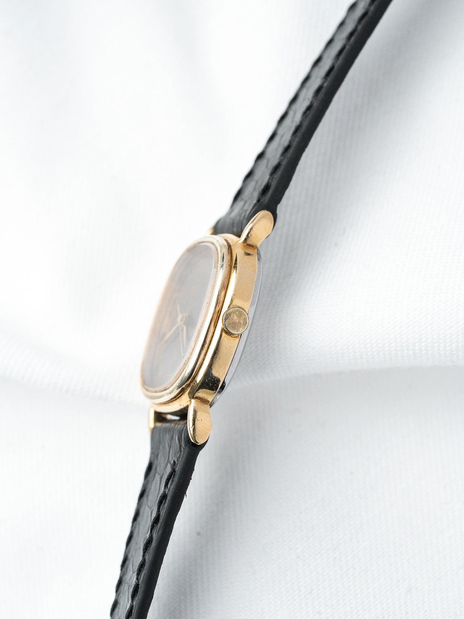 Vintage gold watch with black leather strap, side view on white background