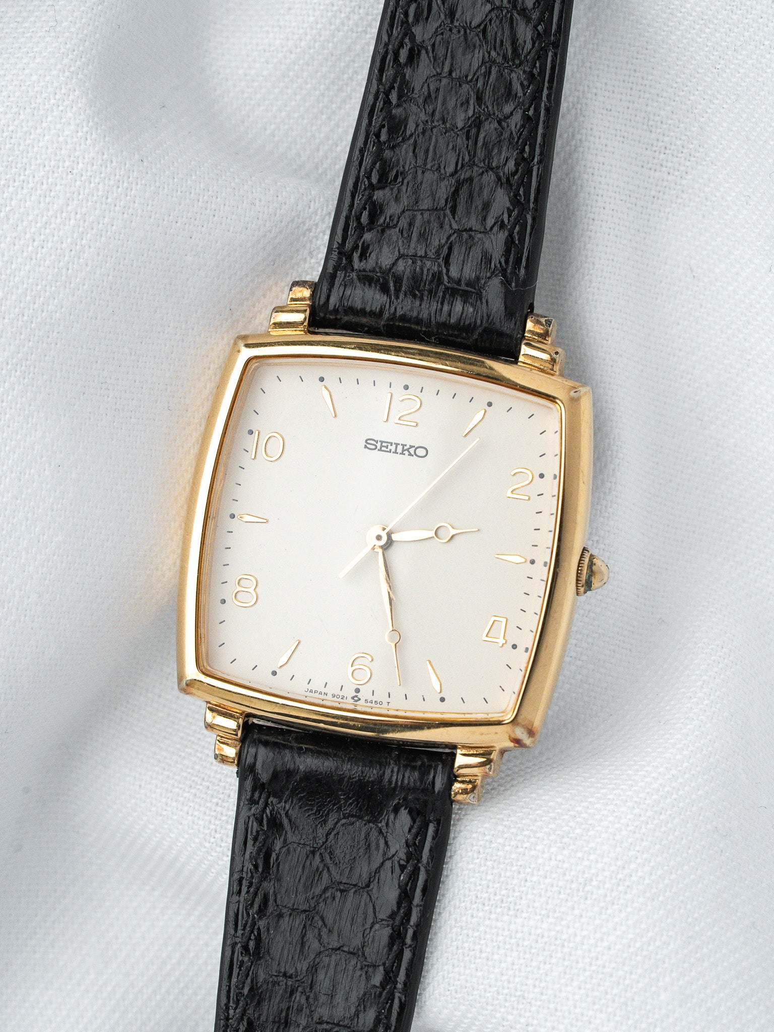 Seiko vintage watch with gold case, white dial, black alligator strap on white fabric