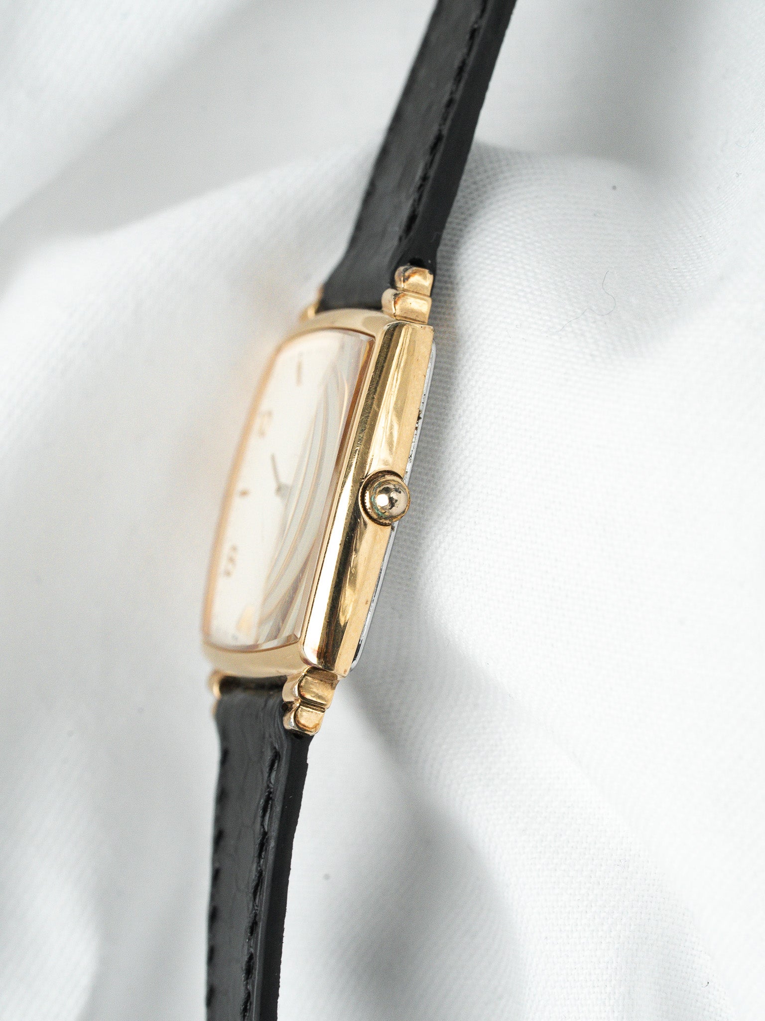 Vintage Cartier watch with gold case, white dial, black leather strap on white fabric
