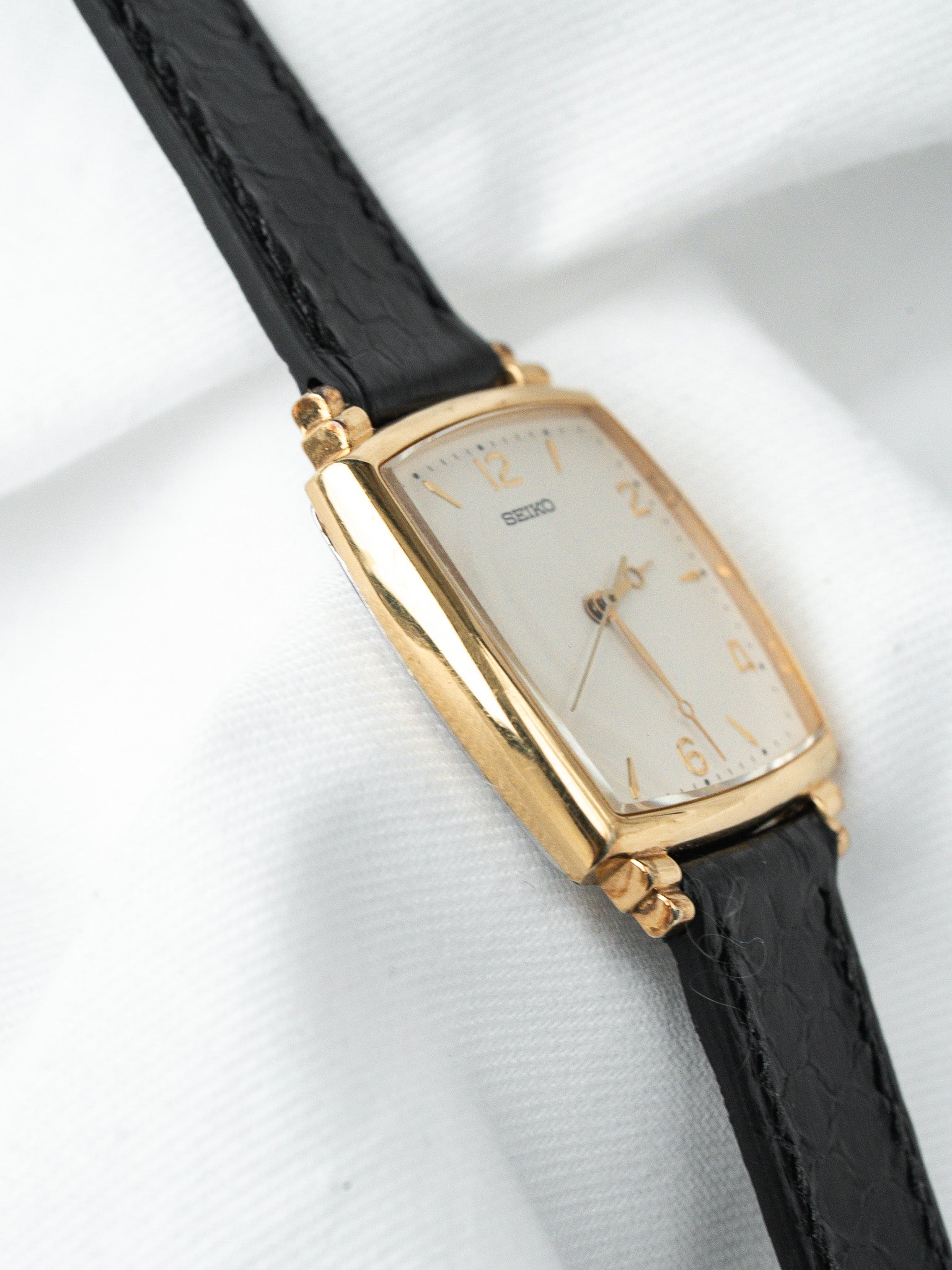Seiko vintage watch with gold case, white dial, black leather strap on white fabric