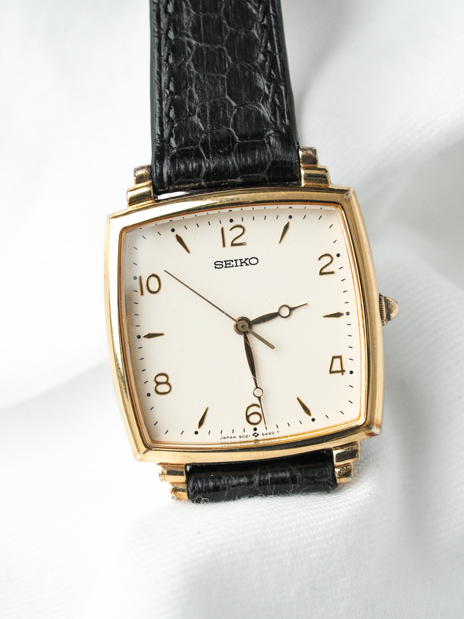 Seiko vintage watch with gold case, white dial, black leather strap on white background