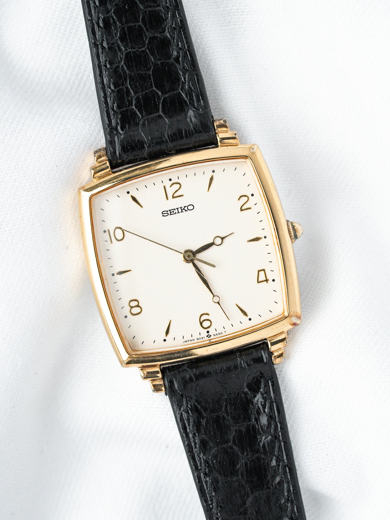 Seiko vintage watch with gold case, white dial, black crocodile strap on white background