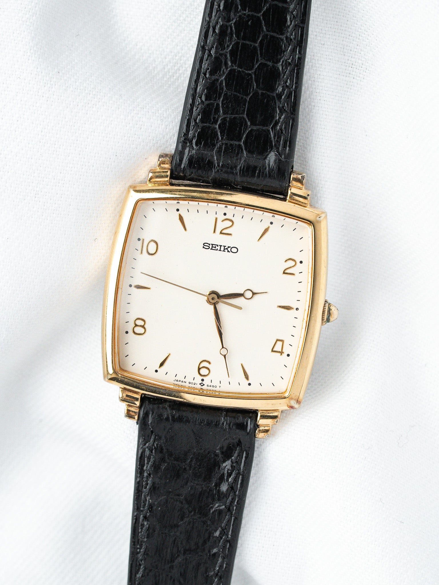 Seiko vintage watch with gold case, white dial, black crocodile strap on white background