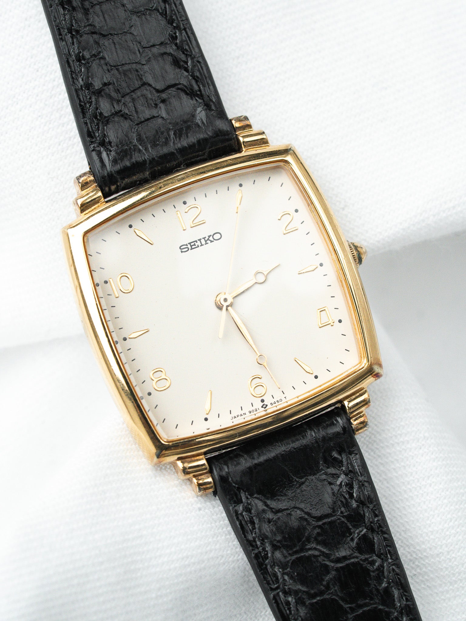 Seiko vintage watch with gold case, white dial, black crocodile strap on white background