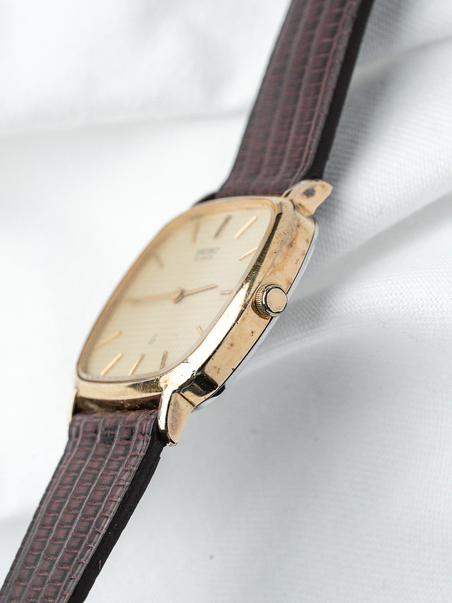 Vintage Universal Genève watch with gold case, cream dial, brown textured strap on white fabric