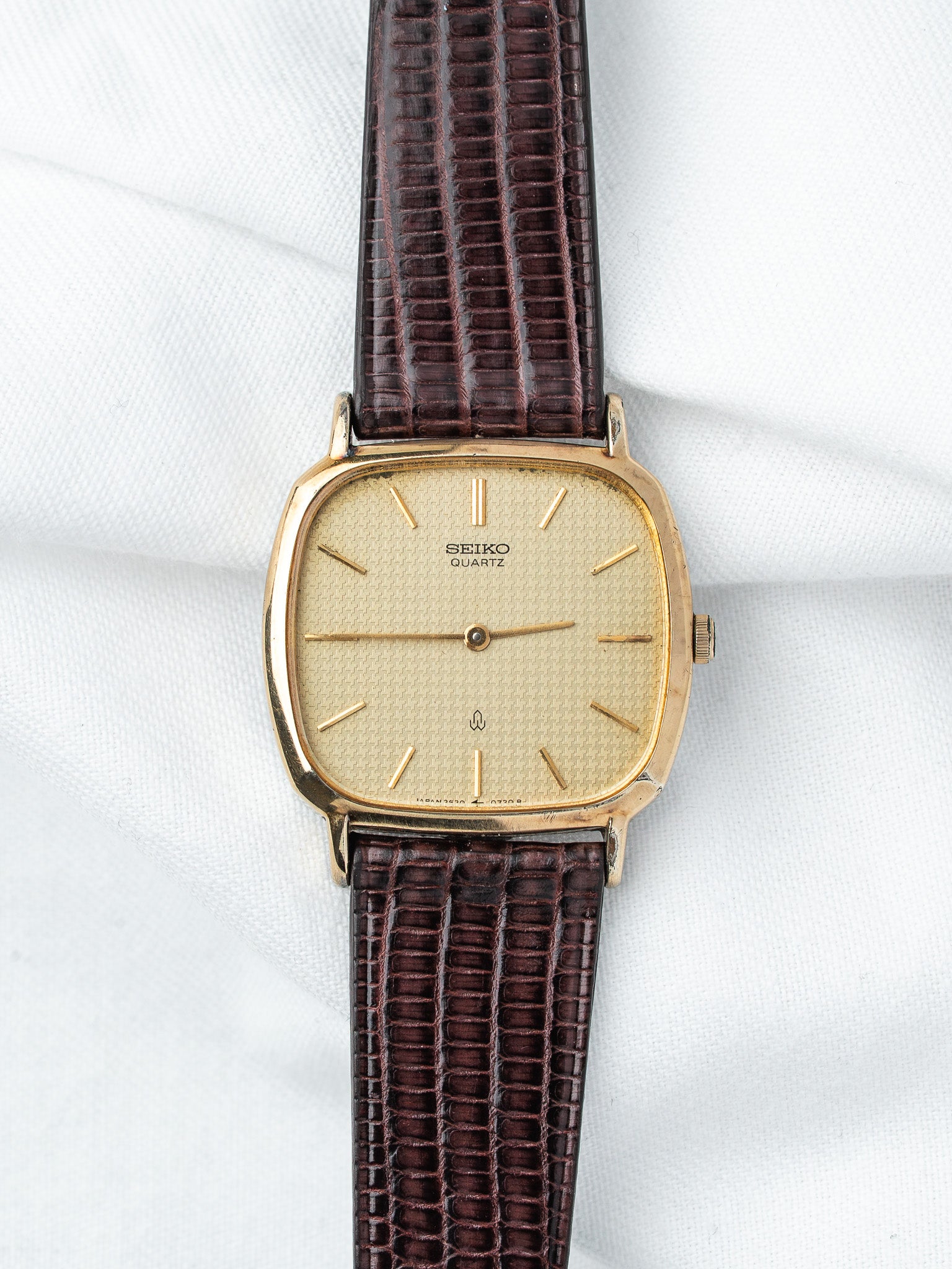 Seiko Quartz vintage watch with gold case, cream dial, brown lizard strap on white fabric