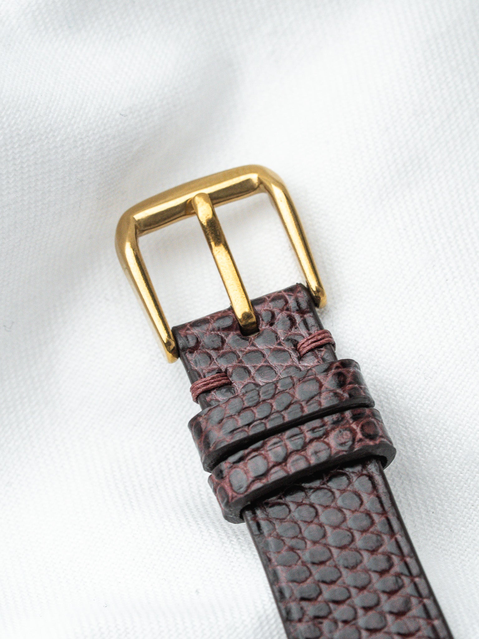 Vintage watch strap with textured burgundy leather and gold buckle on white background