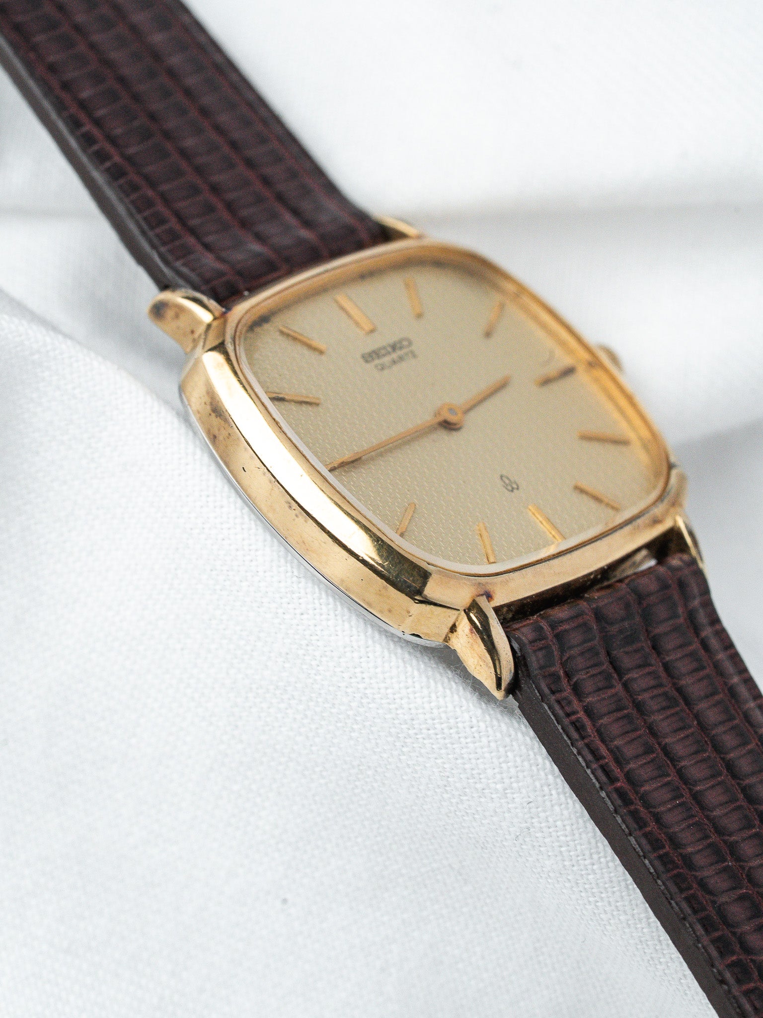 Seiko vintage watch with gold case, cream dial, and brown textured strap on white fabric