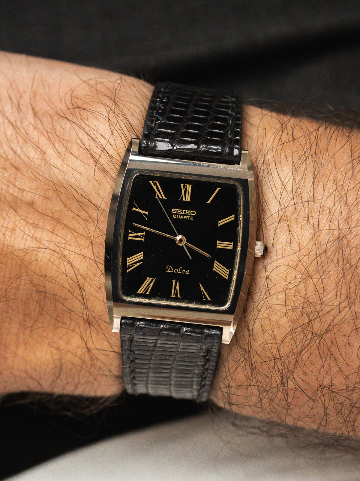 Montre Seiko Dolce vintage avec cadran noir, index romains dorés et bracelet cuir noir.