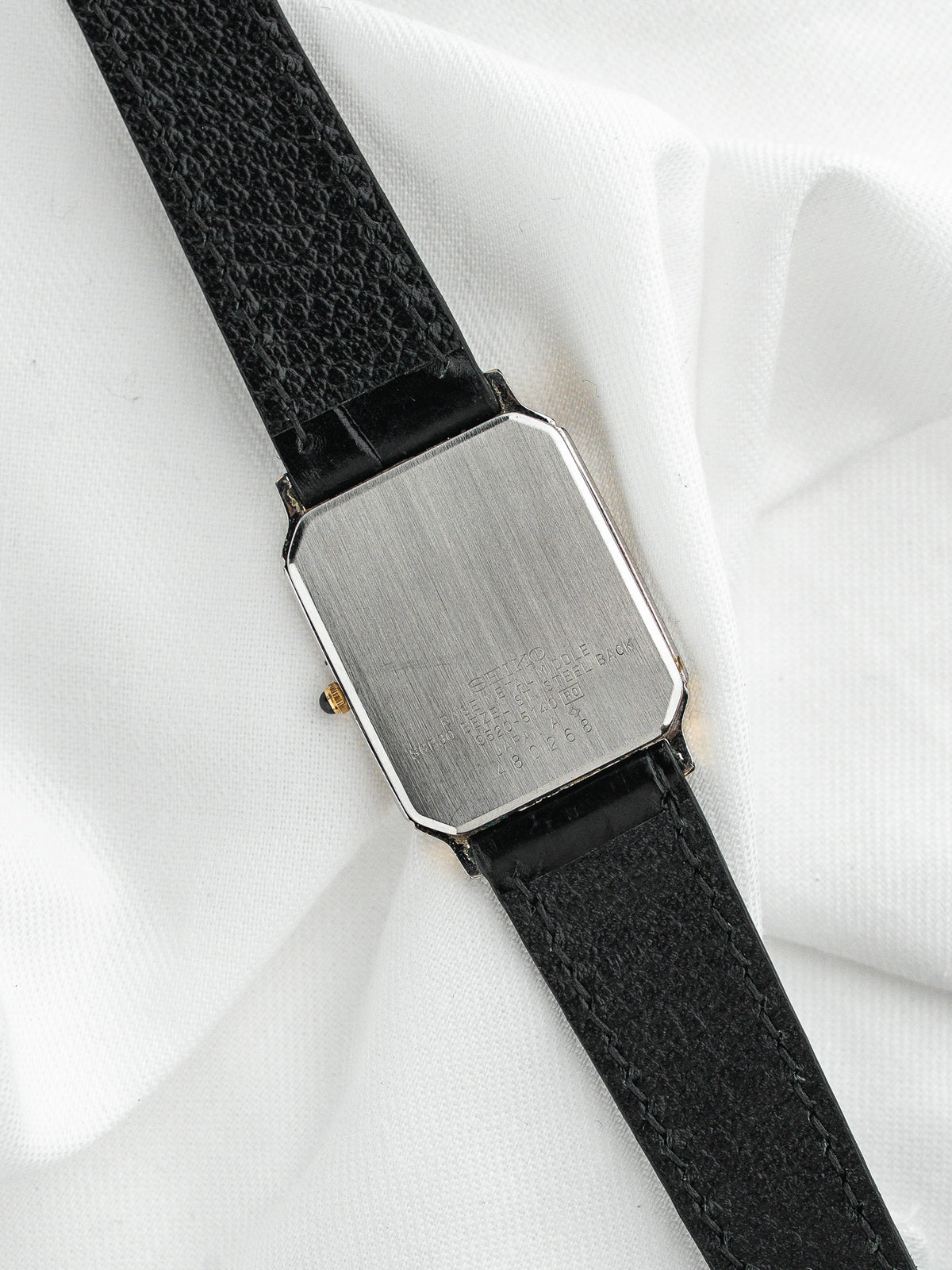 Dos d'une montre vintage au boîtier rectangulaire en acier avec bracelet cuir noir