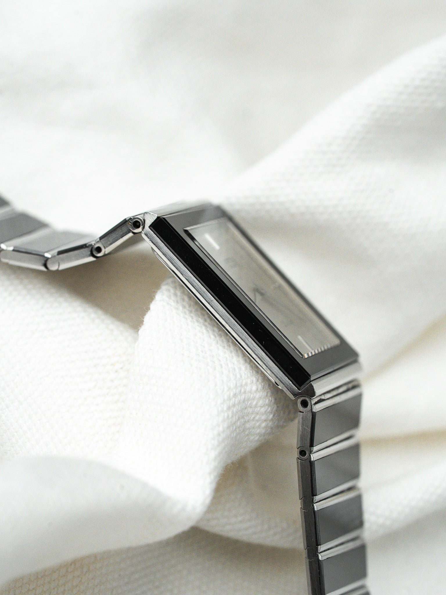 Vintage Cartier watch with rectangular case, black dial, and steel bracelet on white fabric