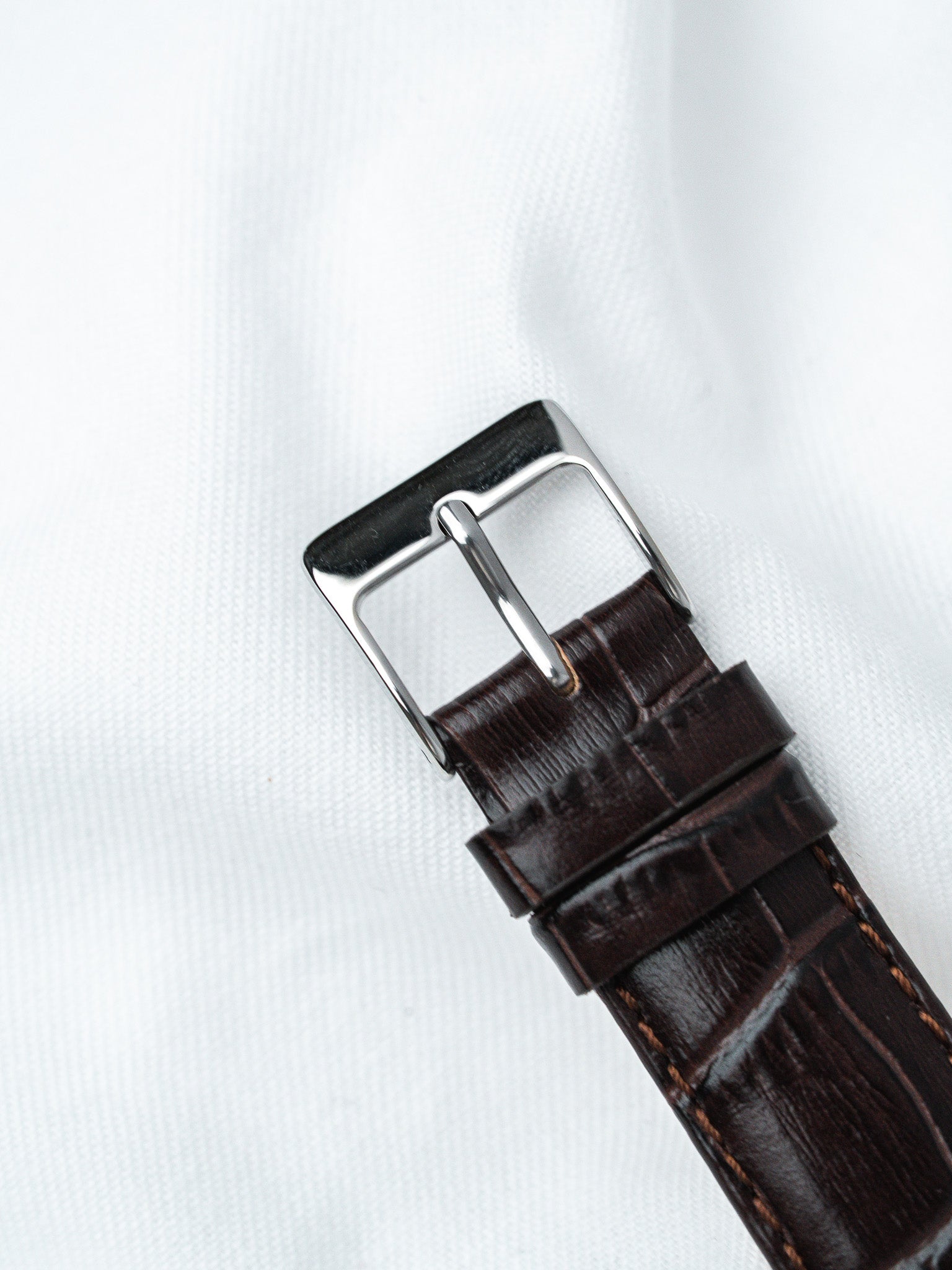 Brown alligator leather watch strap with polished steel buckle on white fabric