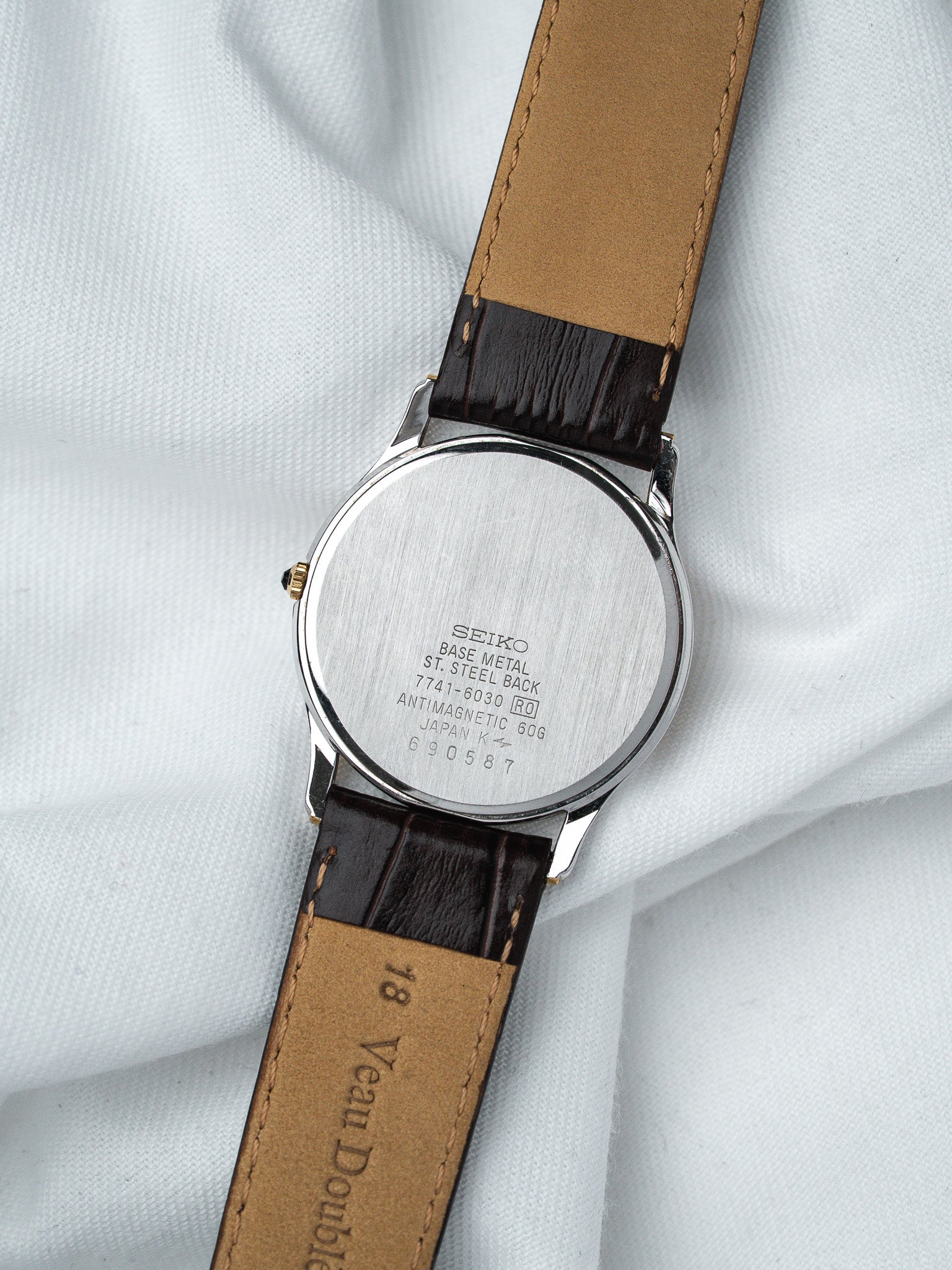Seiko vintage watch with stainless steel back, brown leather strap, displayed on white fabric