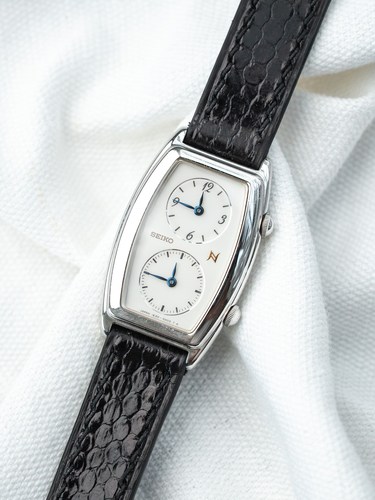 Seiko vintage watch with white dial, blue hands, black textured strap on white fabric