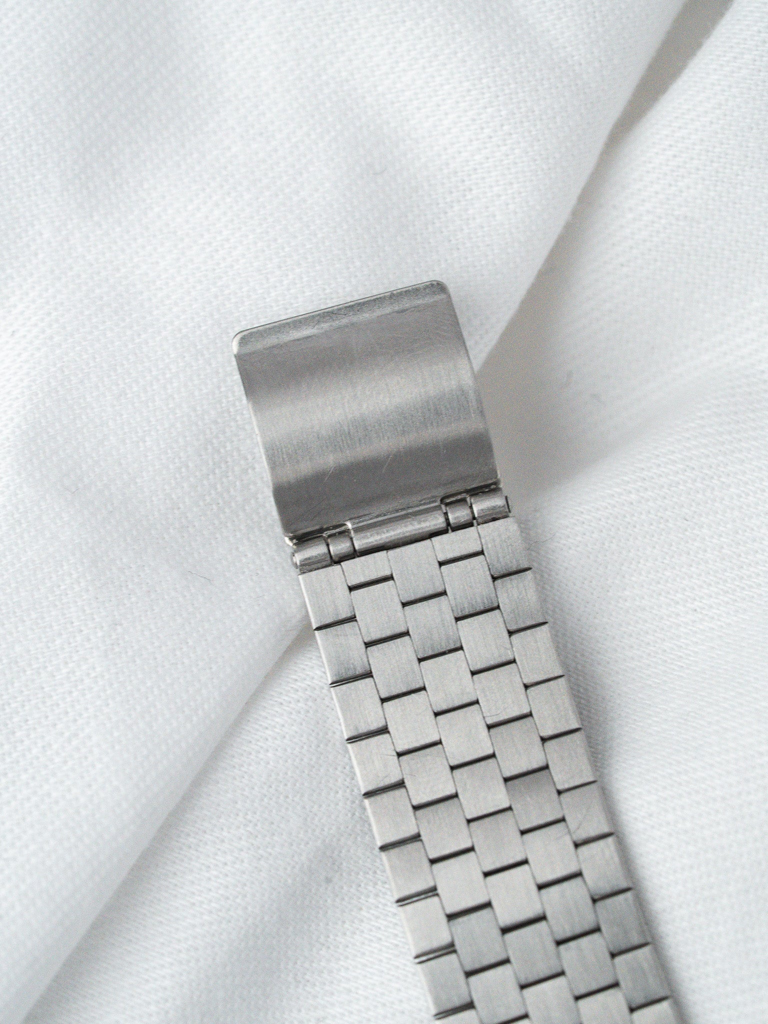 Stainless steel watch bracelet with mesh design, resting on white fabric