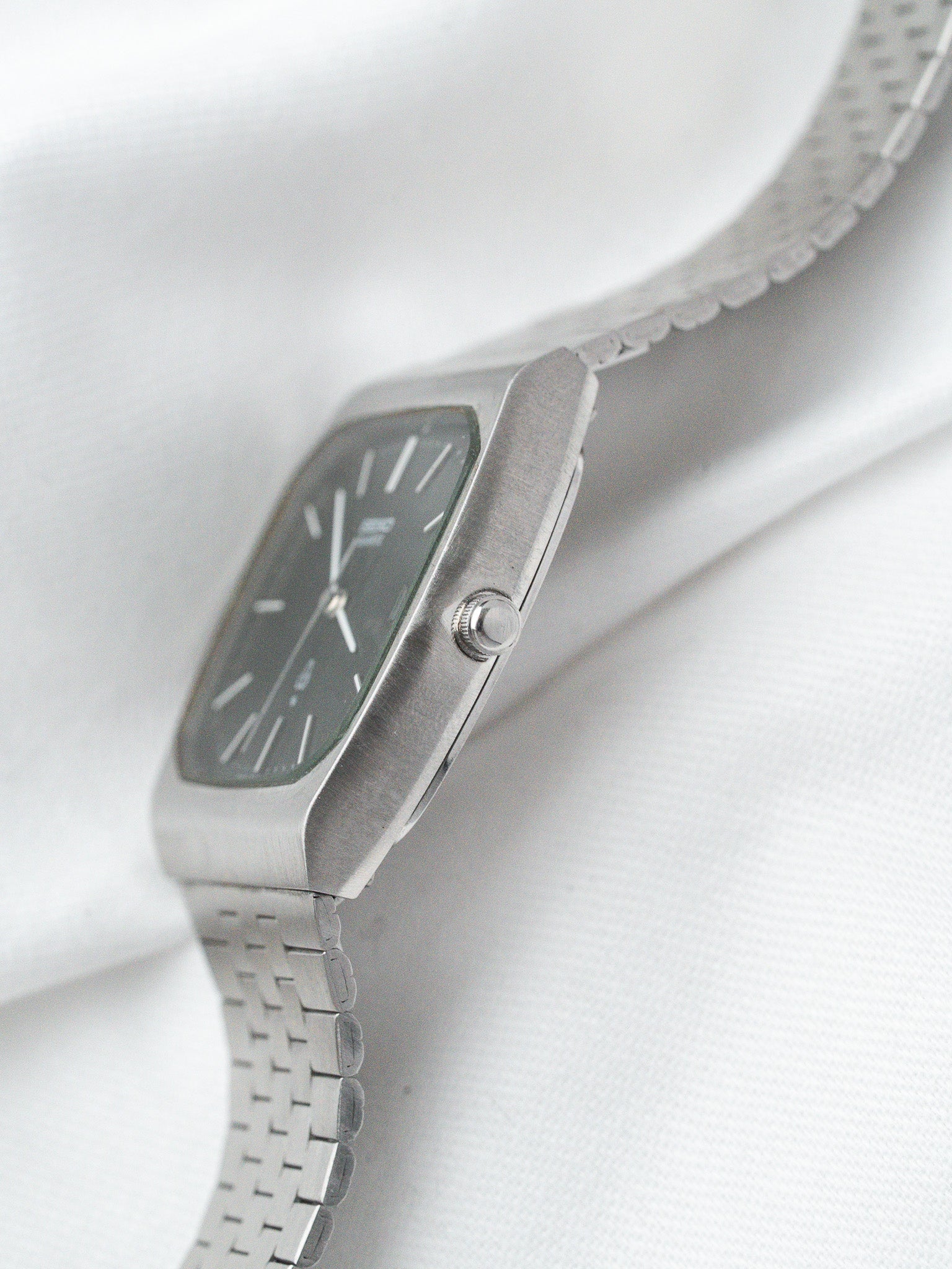Seiko vintage watch with rectangular case, dark dial, and steel mesh bracelet on white fabric