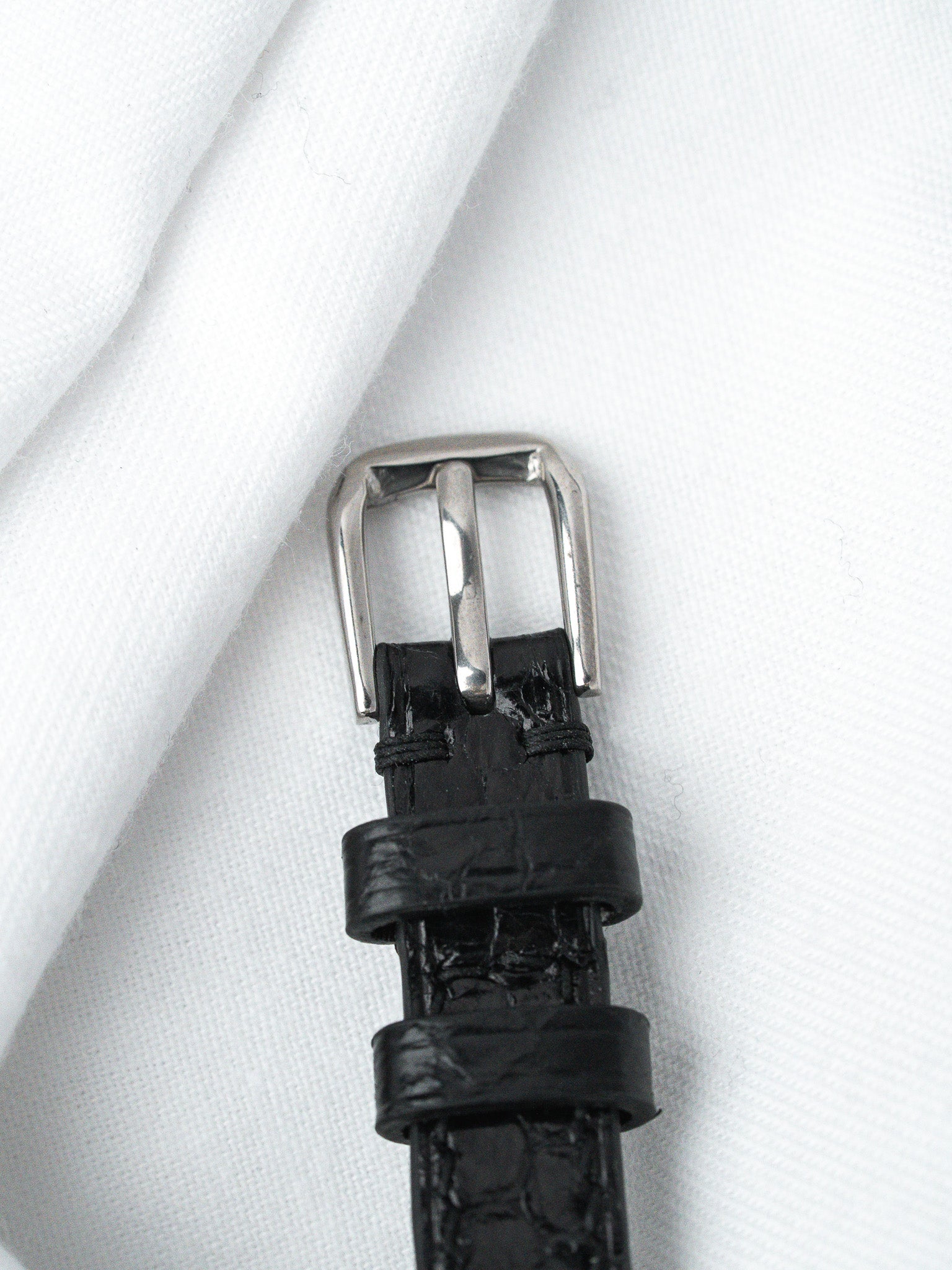 Black alligator leather watch strap with silver buckle on white fabric