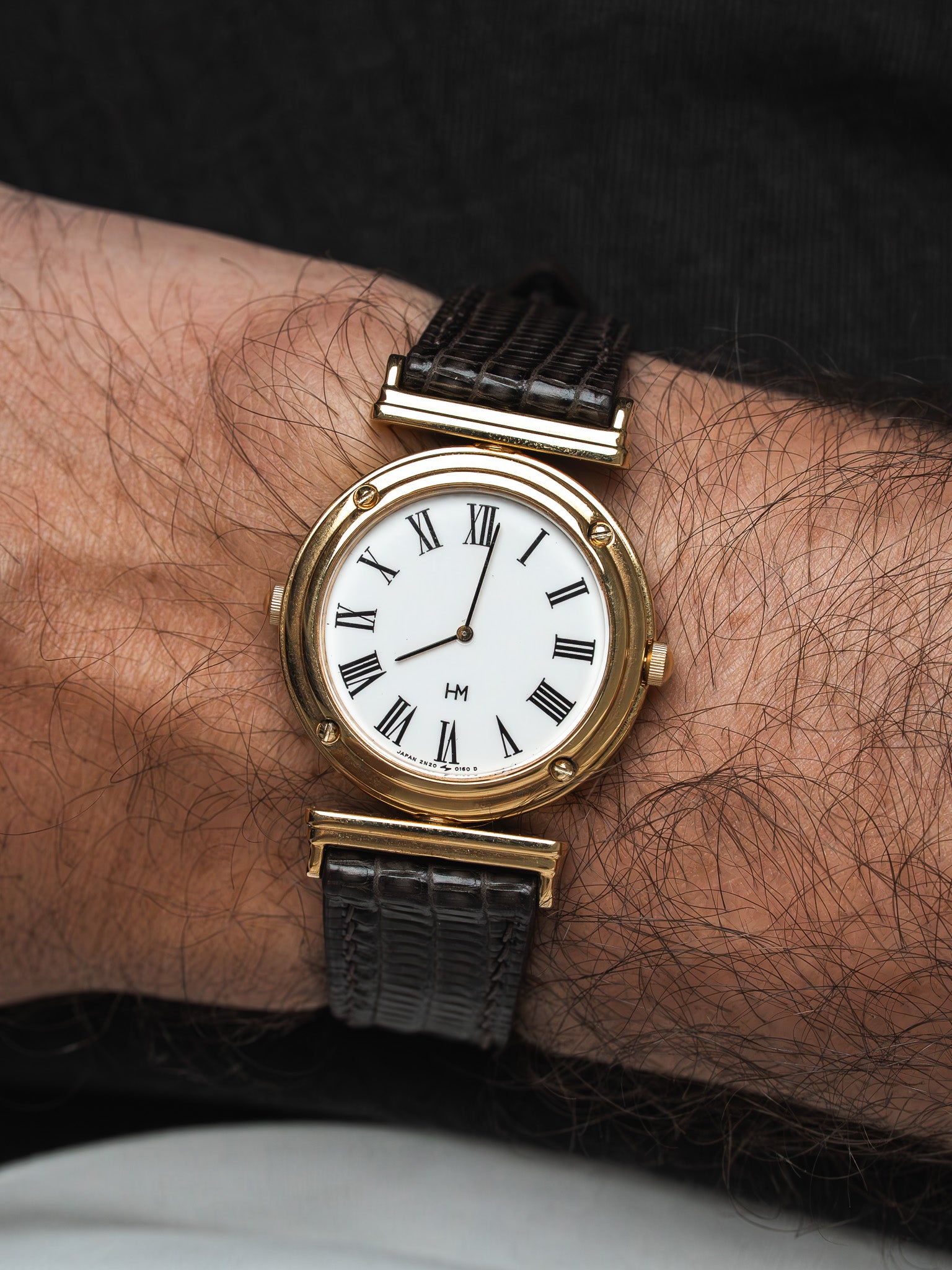 Vintage HM watch with gold case, white dial, Roman numerals, black leather strap on wrist