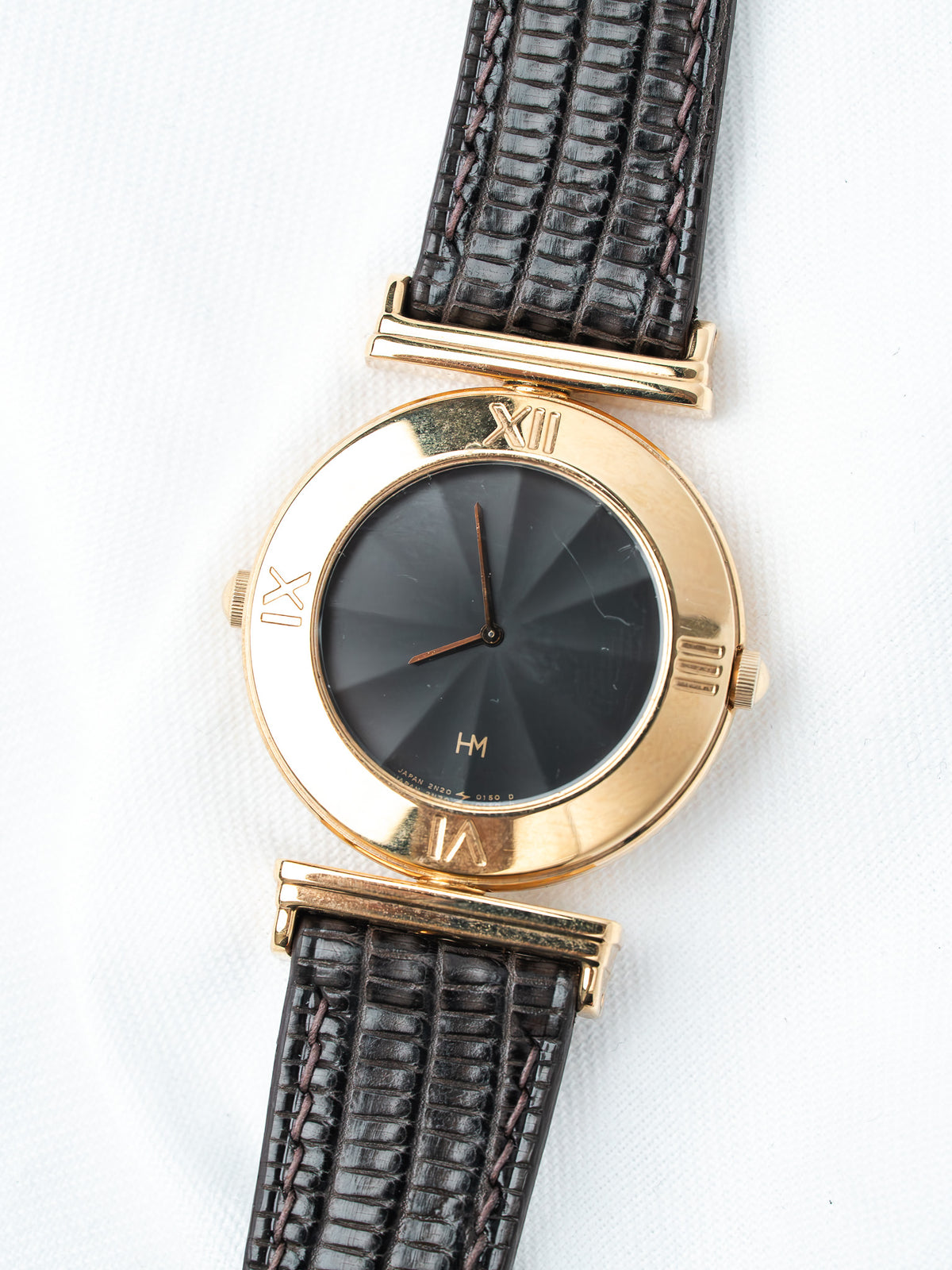 Vintage HM watch with gold case, black sunburst dial, Roman numerals, and dark lizard strap