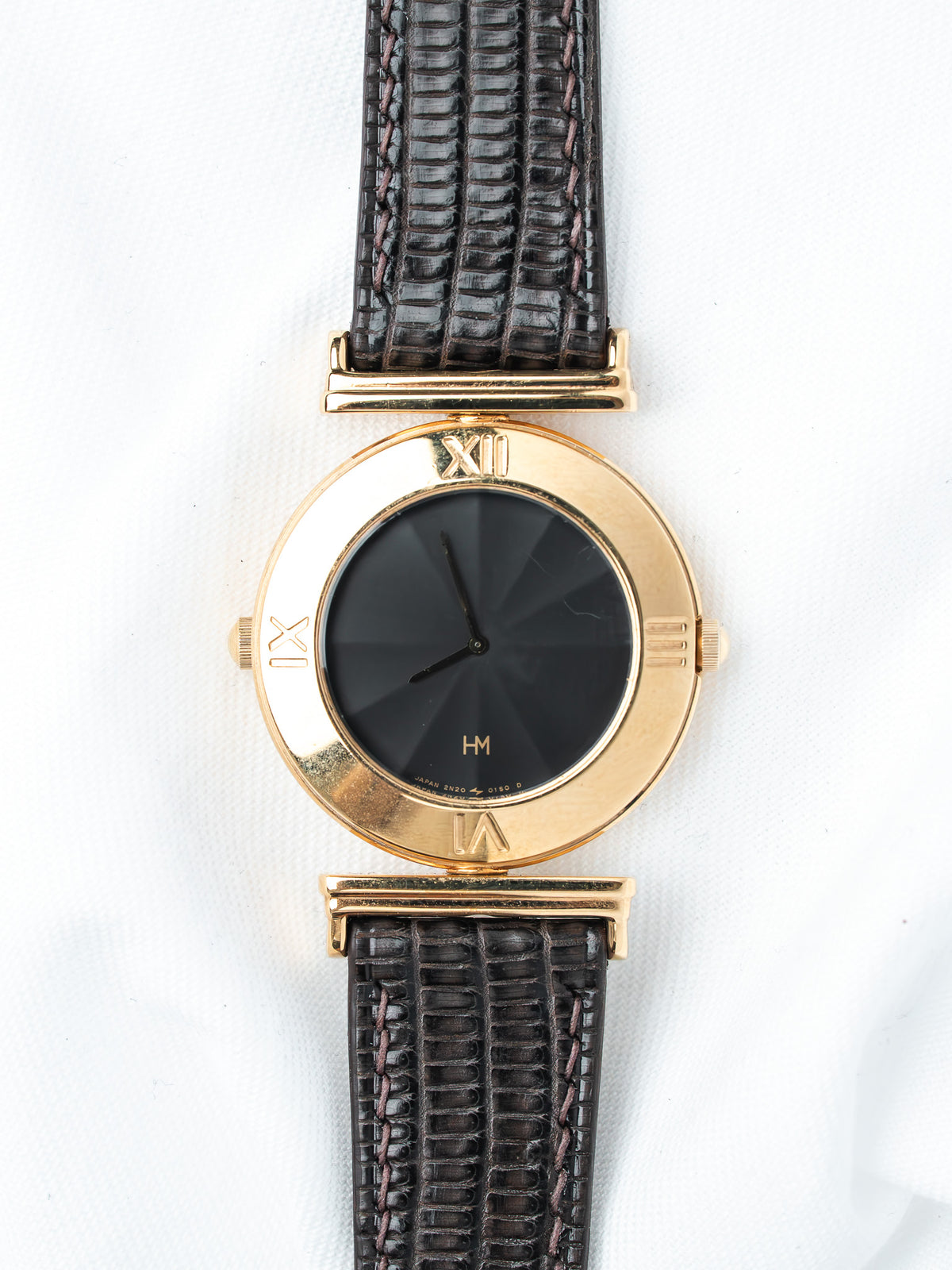 Vintage HM watch with gold case, black dial, Roman numerals, and dark lizard strap on white background