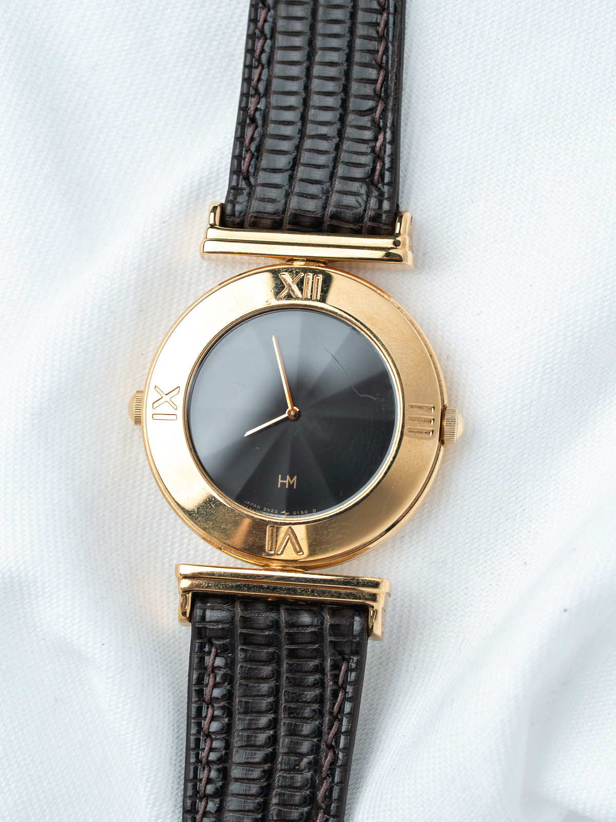 Vintage HM watch with gold case, black dial, Roman numerals, and dark textured strap on white background