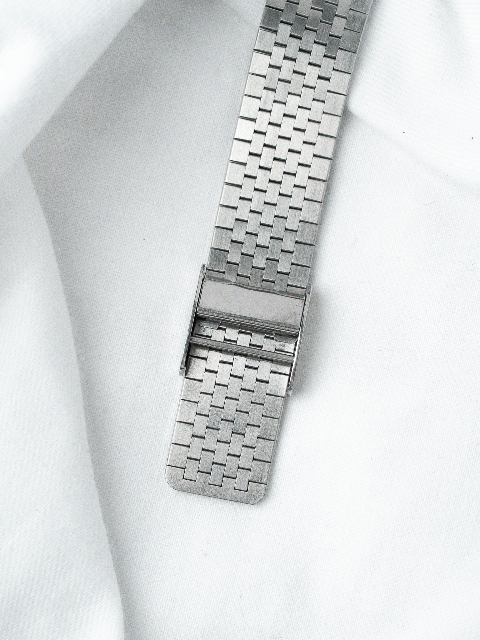 Vintage stainless steel watch bracelet with woven link design on white fabric