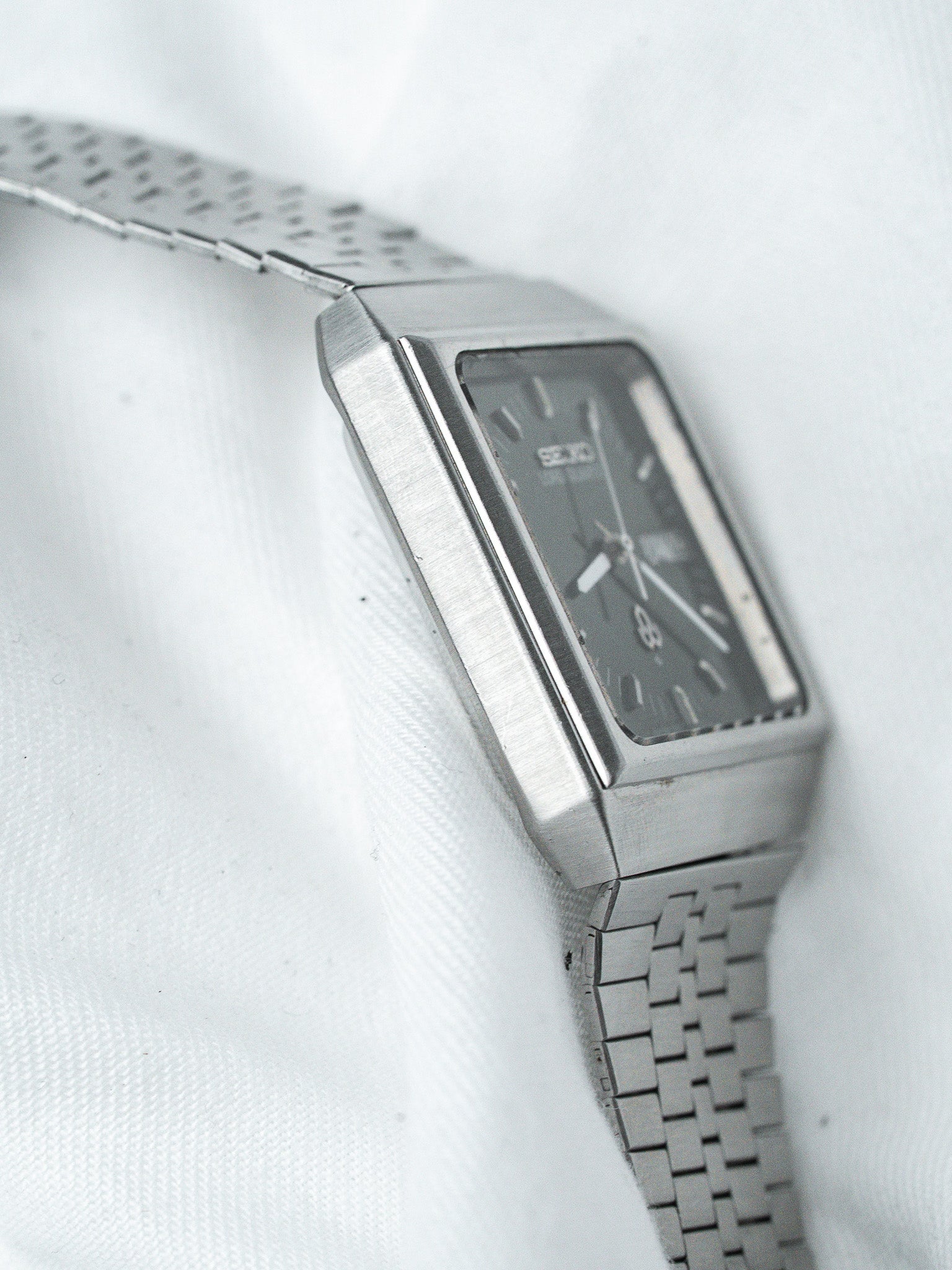Seiko vintage watch with rectangular case, dark dial, and metal bracelet on white fabric