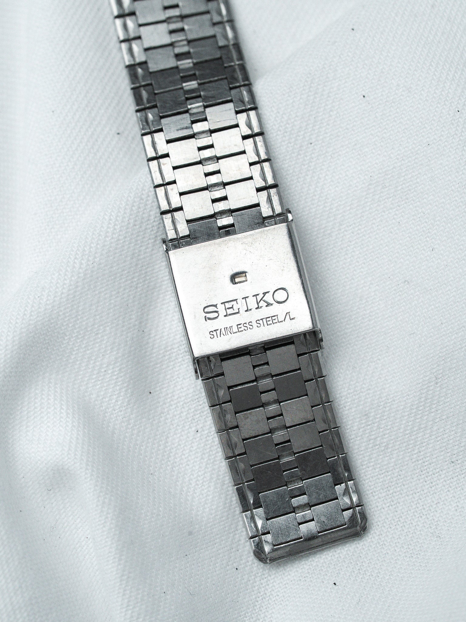 Seiko stainless steel watch bracelet with geometric link design on white background