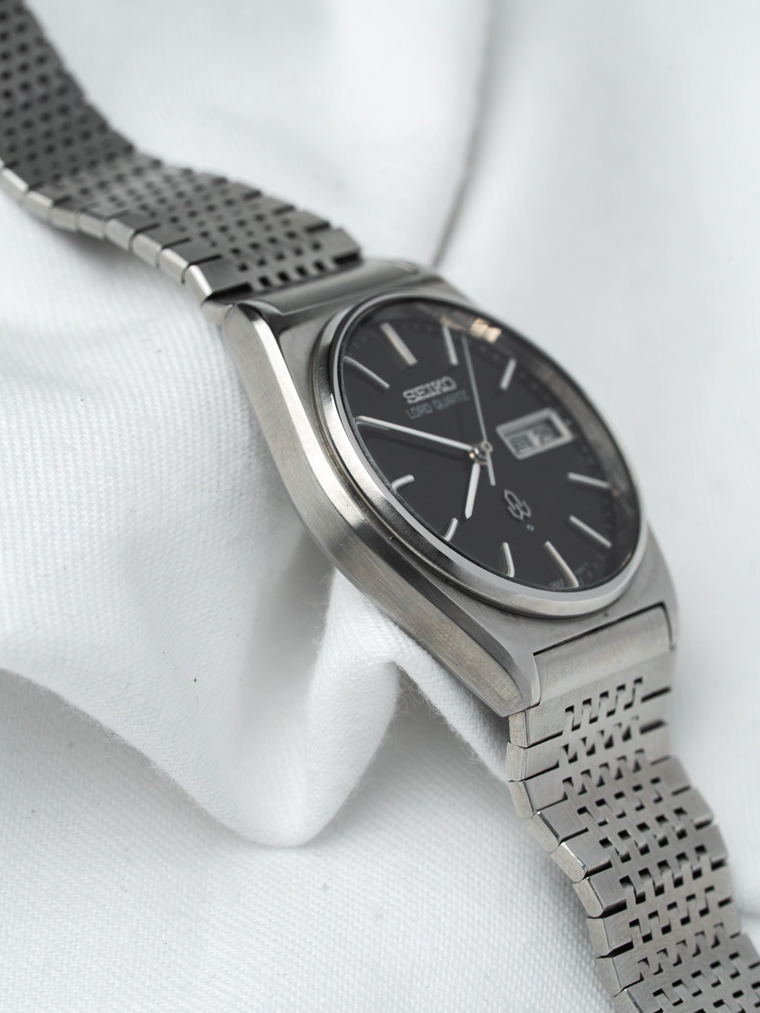 Seiko 5 vintage watch with black dial and stainless steel mesh bracelet on white fabric