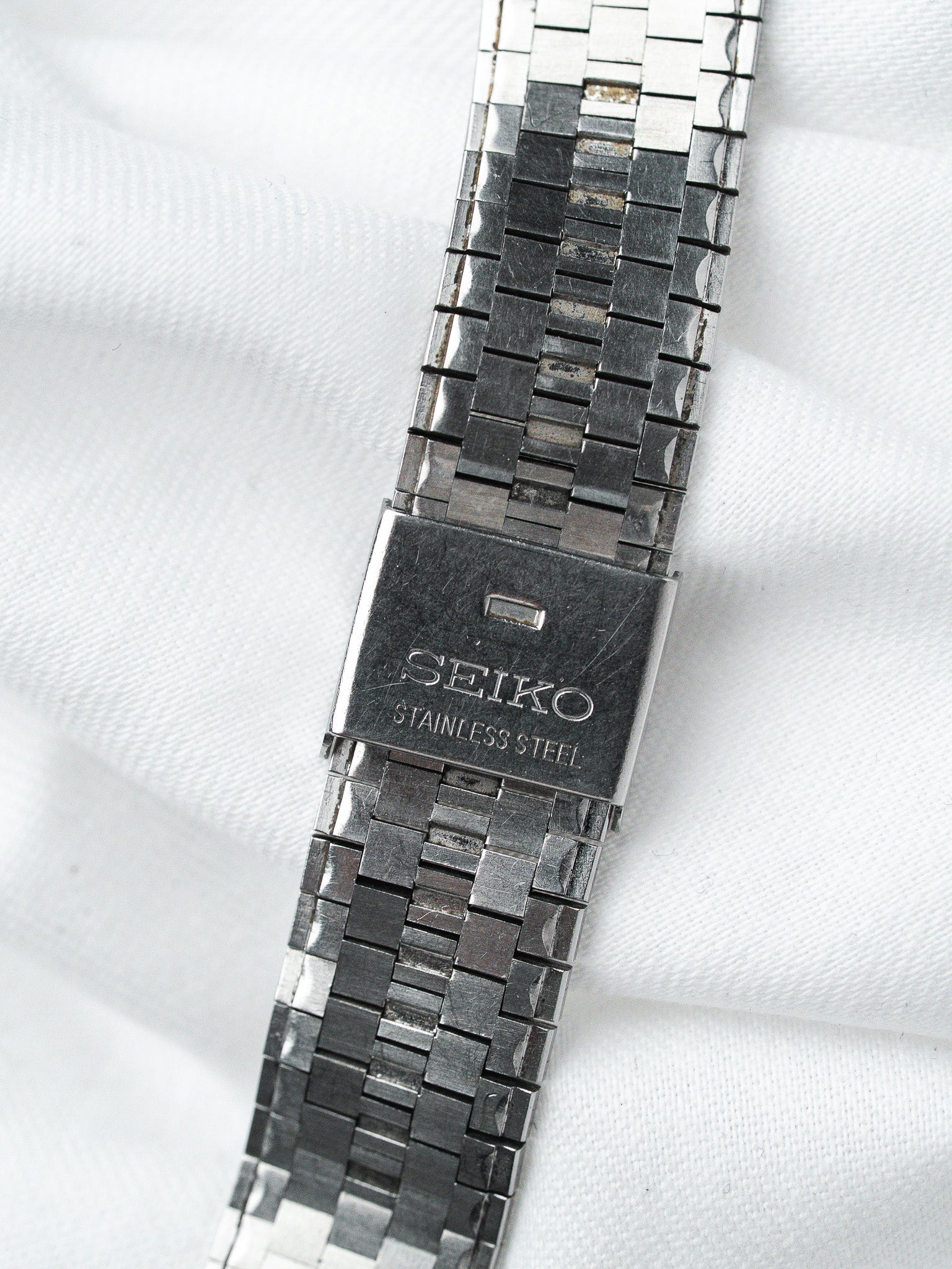 Seiko vintage stainless steel watch bracelet with textured links on white fabric