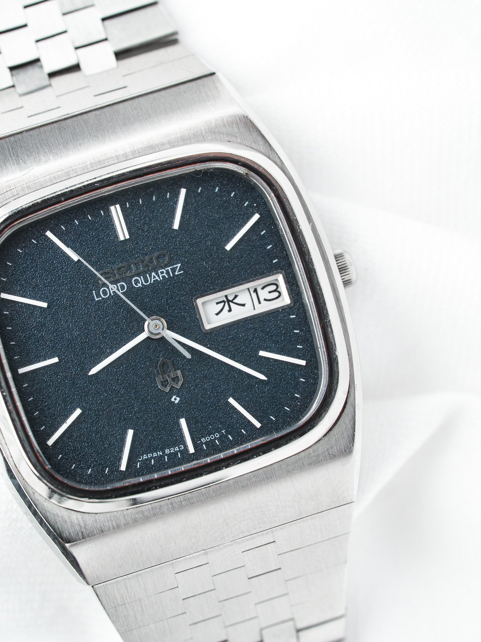 Seiko Lord Quartz vintage watch with dark dial, white markers, and steel bracelet on white background