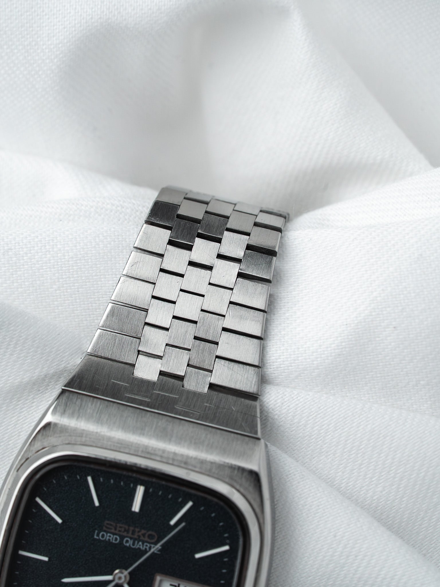 Seiko Lord Quartz vintage watch with black dial and woven steel bracelet on white fabric