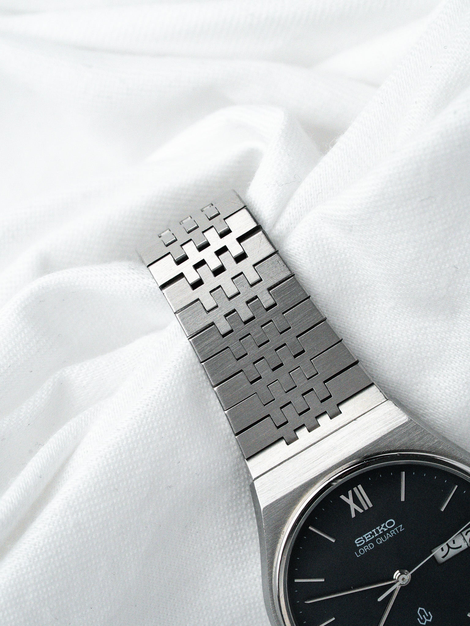 Seiko Lord Quartz vintage watch with black dial and distinctive metal bracelet on white fabric