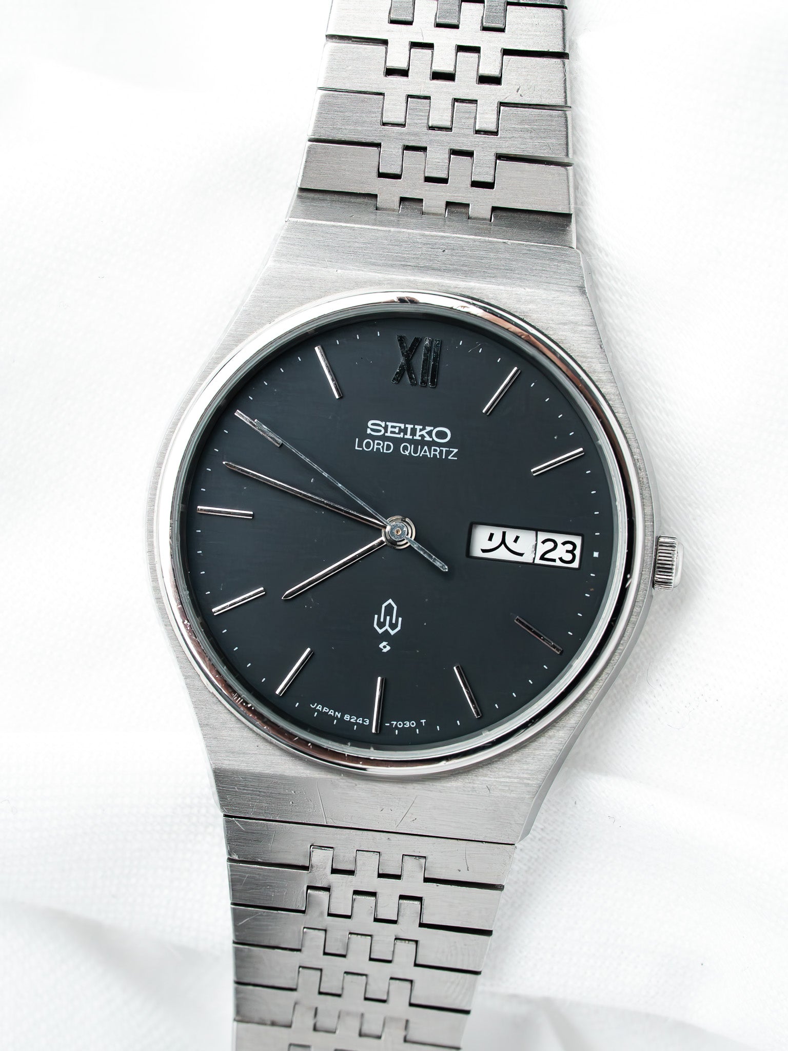 Seiko Lord Quartz vintage watch with black dial, steel case, and patterned bracelet on white background