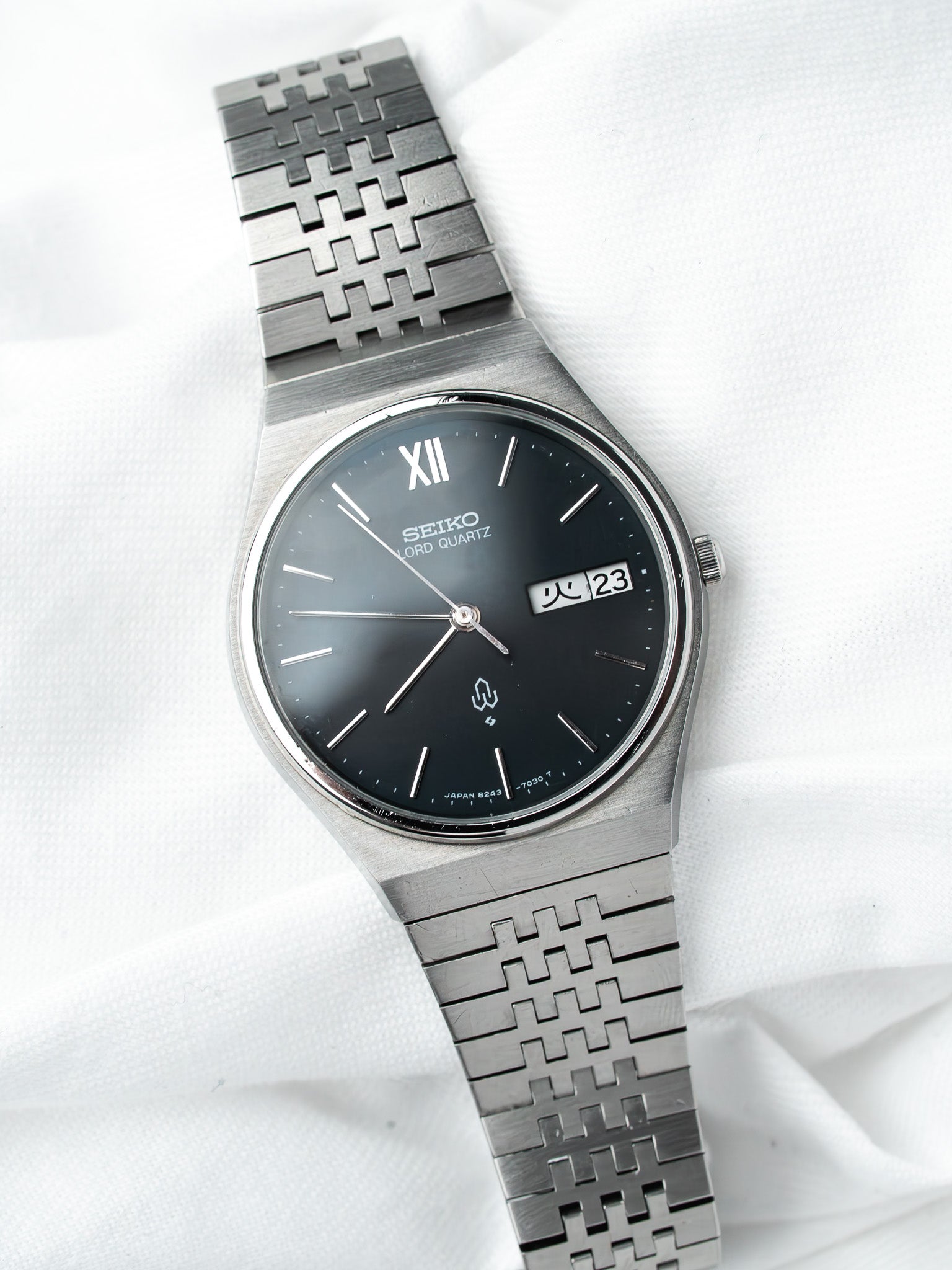 Seiko Lord Quartz vintage watch with black dial, steel case, and patterned bracelet on white fabric