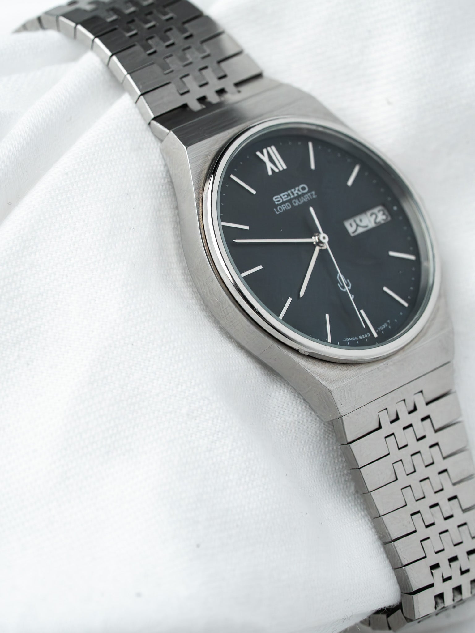 Seiko Lord Quartz vintage watch with black dial, silver case, and patterned metal bracelet on white fabric