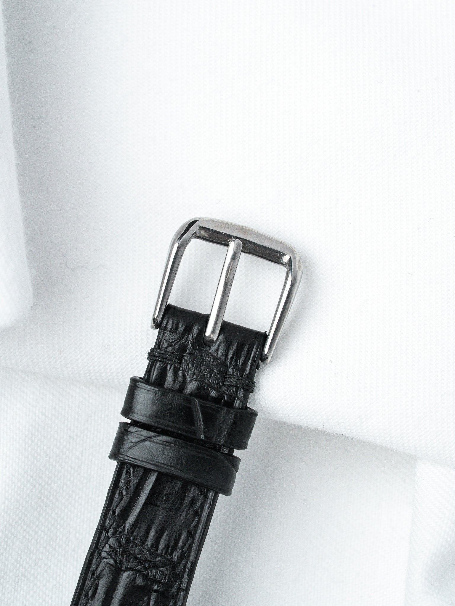 Black alligator leather watch strap with polished steel buckle on white fabric