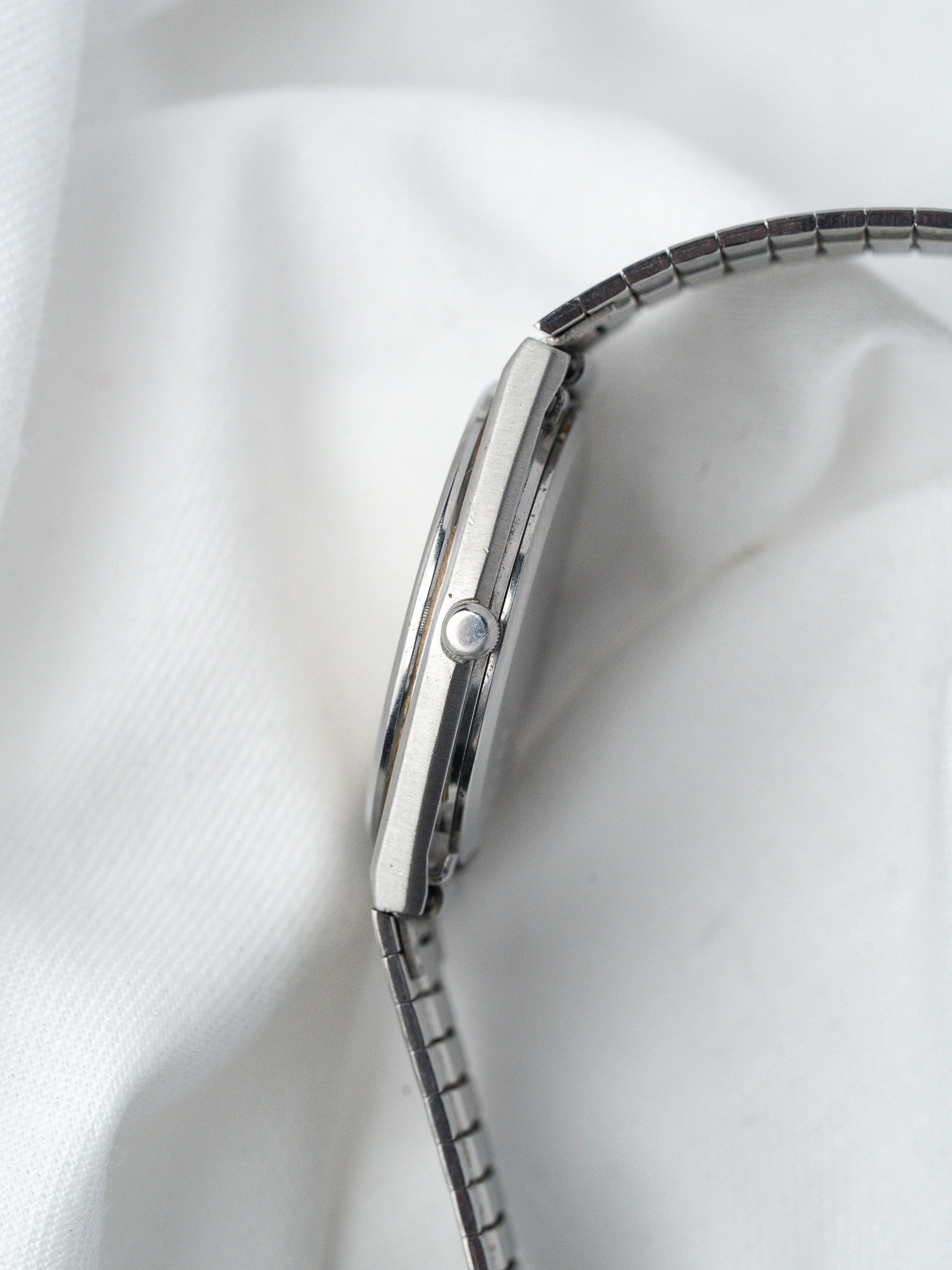 Vintage Omega watch side view, stainless steel case and bracelet on white fabric