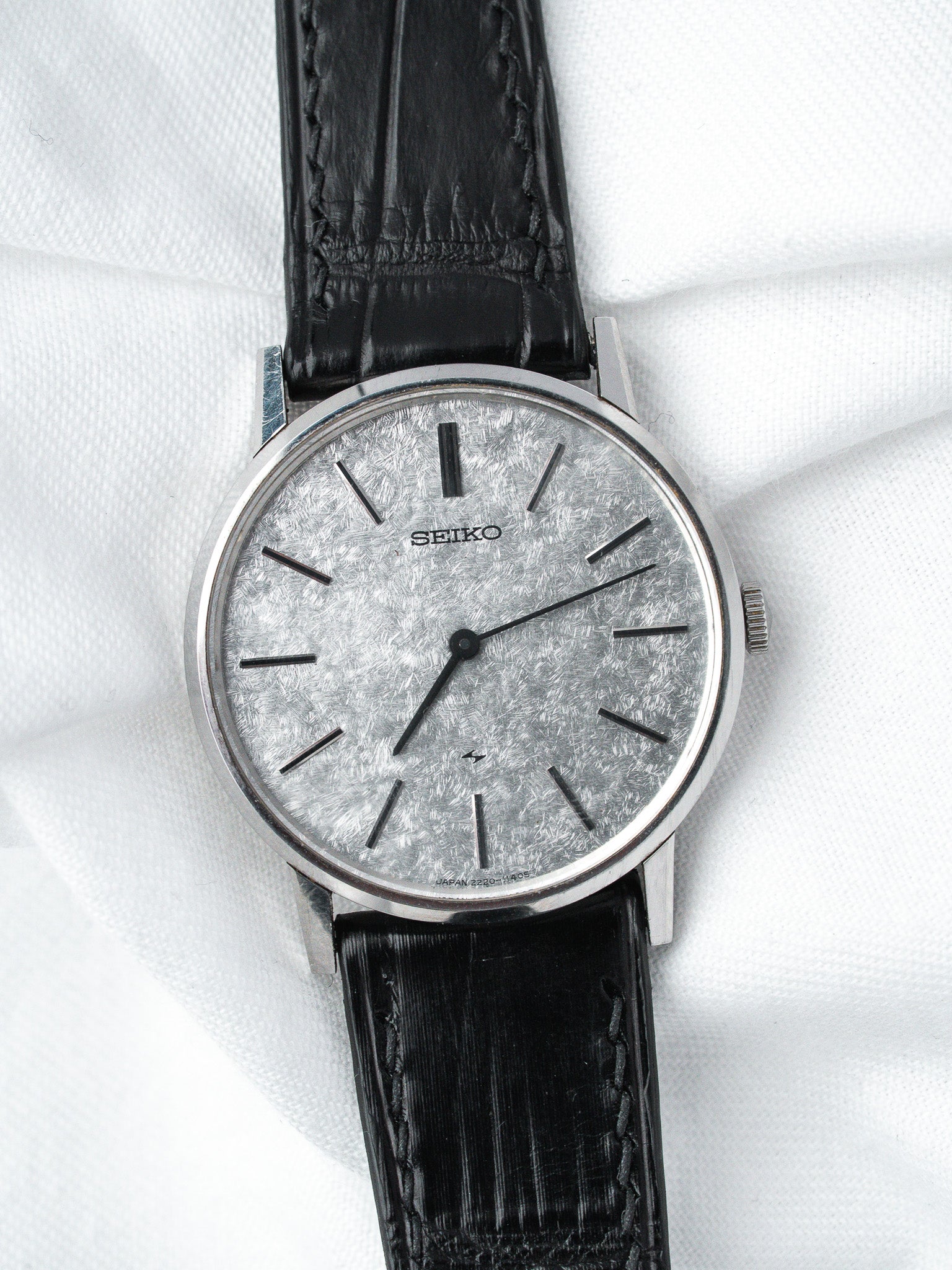 Seiko vintage watch with silver textured dial, black leather strap, on white fabric