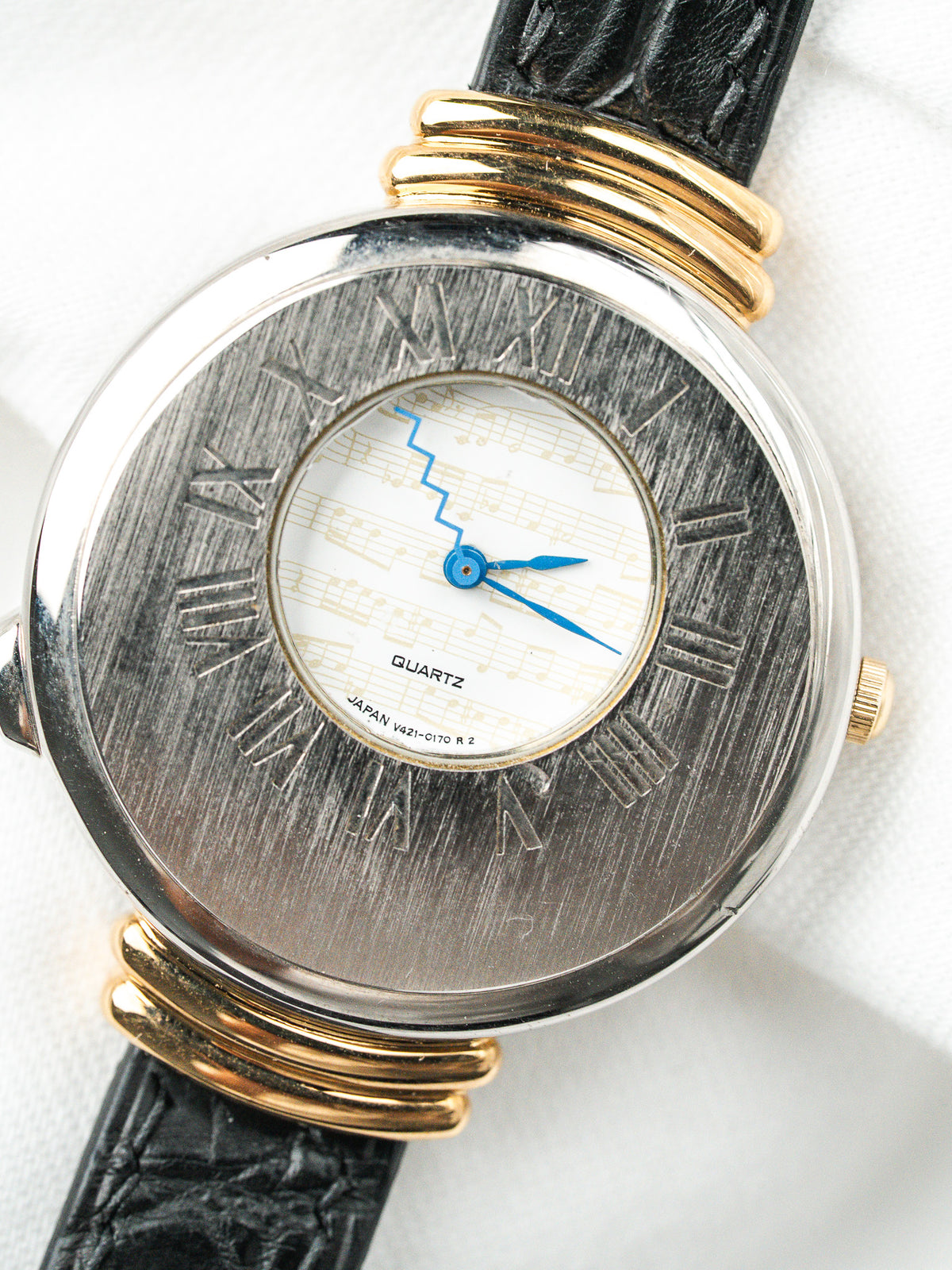 Montre vintage à boîtier rond argenté et doré, cadran partitions et bracelet cuir noir