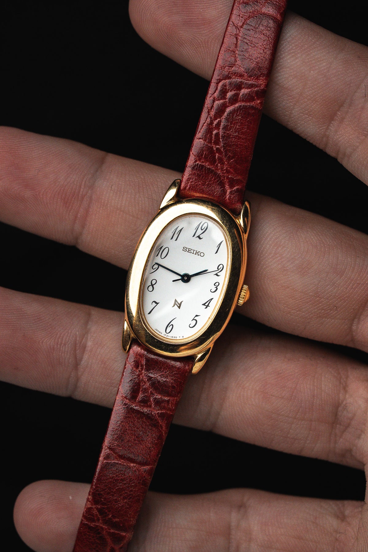 Montre Seiko vintage au boîtier doré ovale et bracelet en cuir rouge croco.