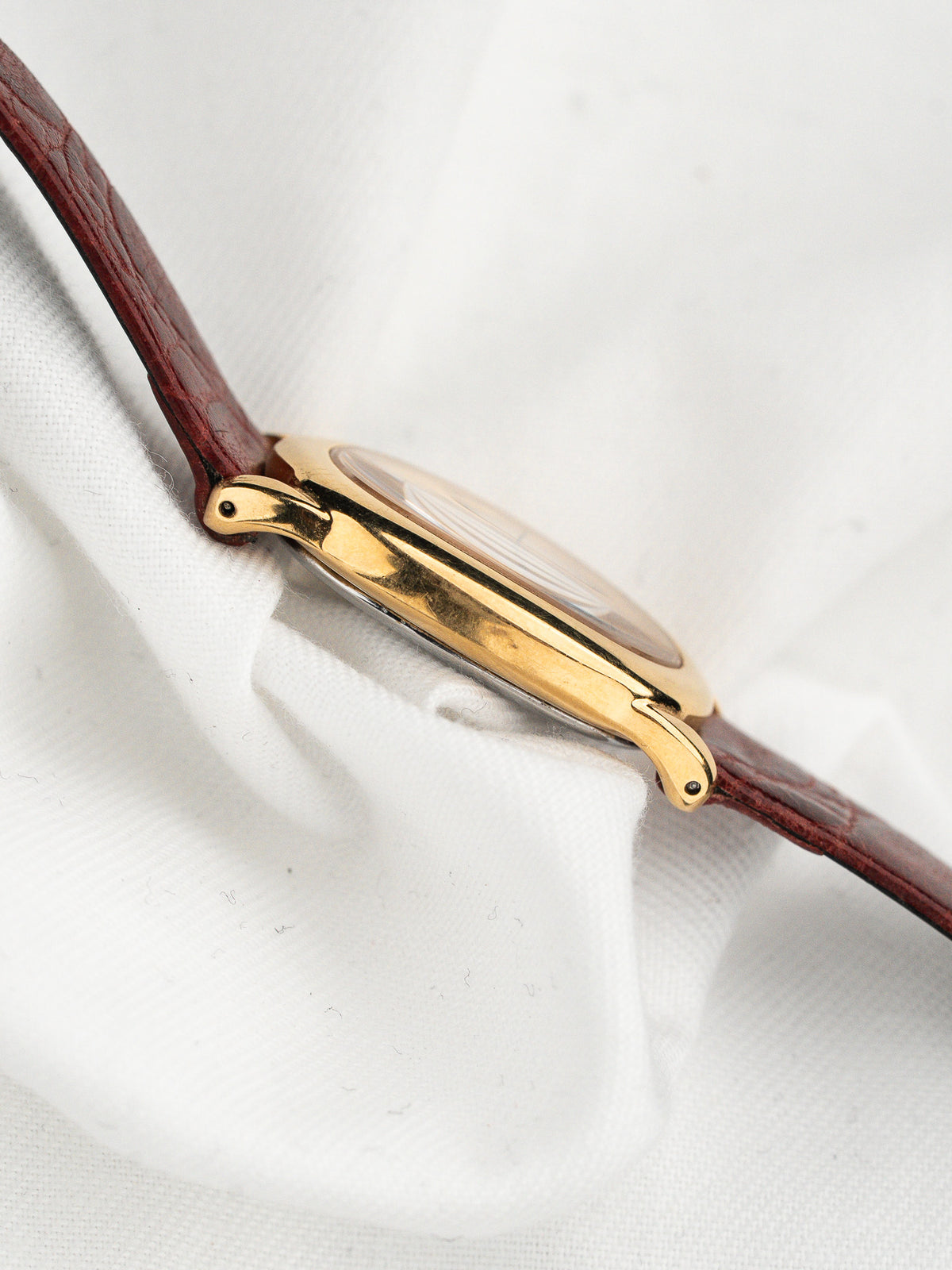 Vue de profil d'une montre vintage dorée avec un bracelet en cuir bordeaux.