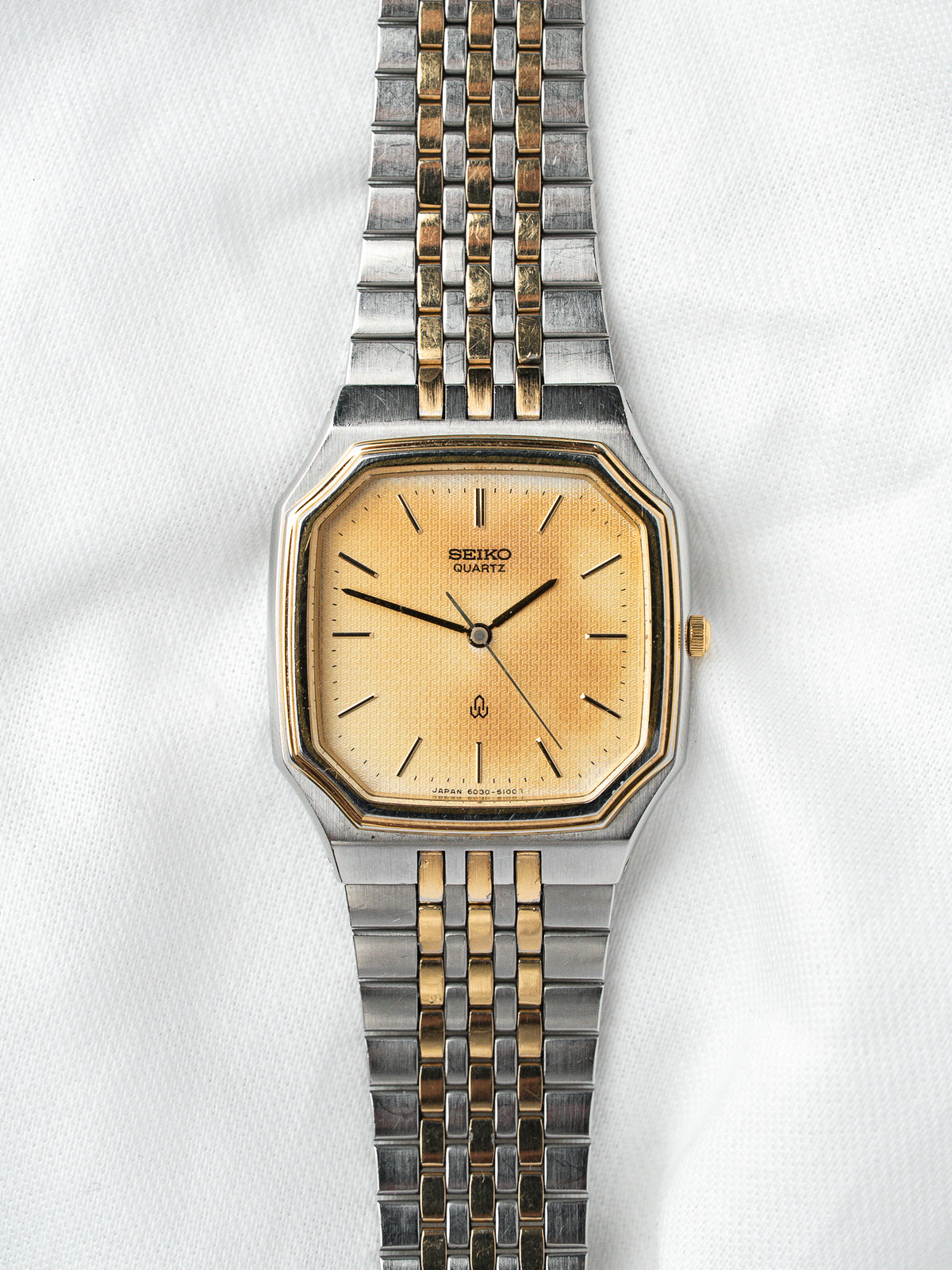 Montre Seiko Quartz vintage, boîtier octogonal doré et bracelet bicolore sur fond blanc
