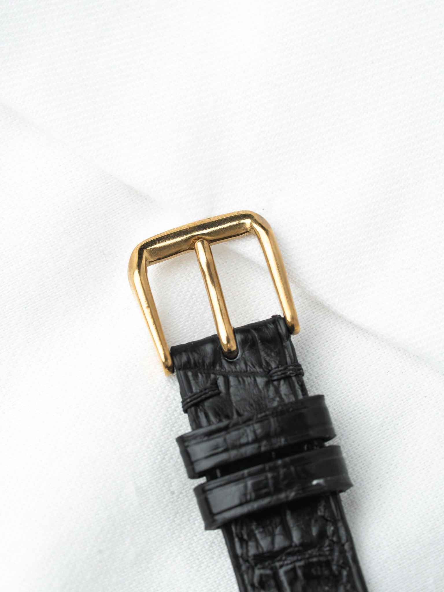 Black alligator leather watch strap with gold buckle on white fabric