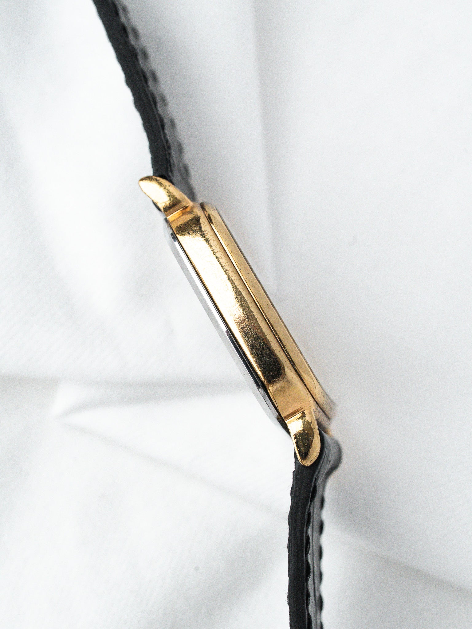 Vintage Cartier Tank watch with gold case and black leather strap on white background