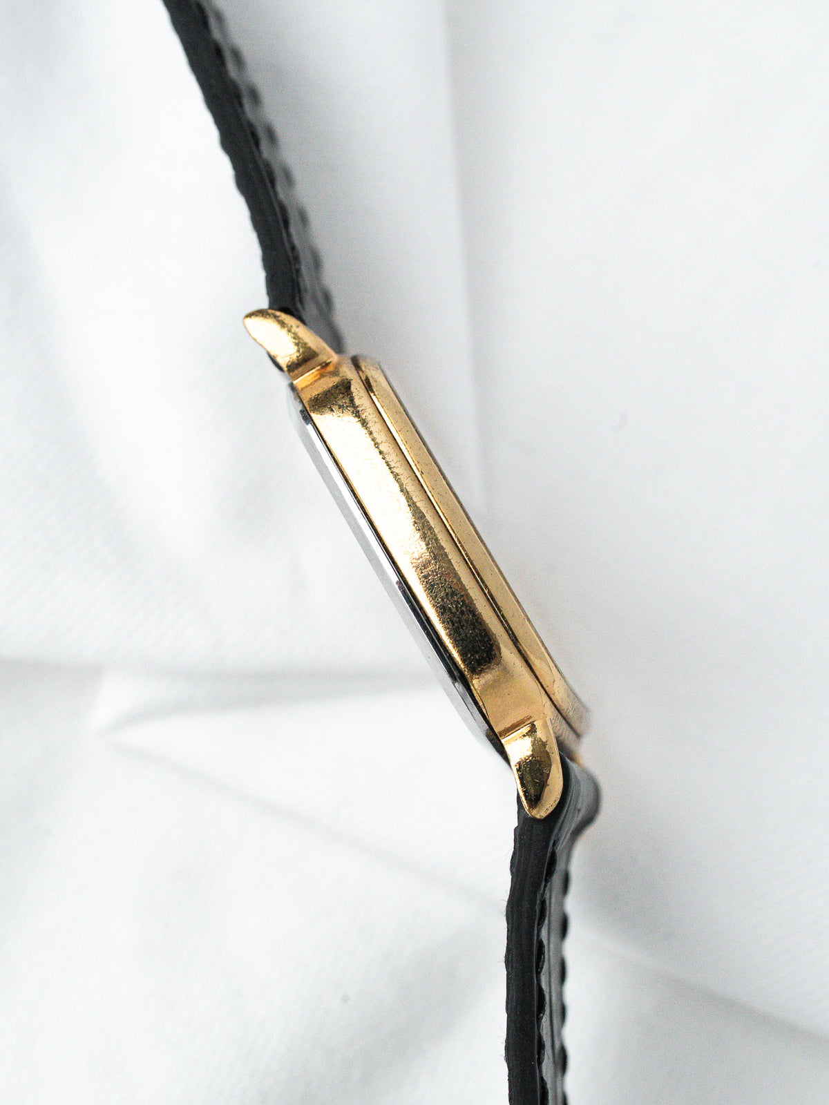 Vintage Cartier Tank watch with gold case and black leather strap on white background